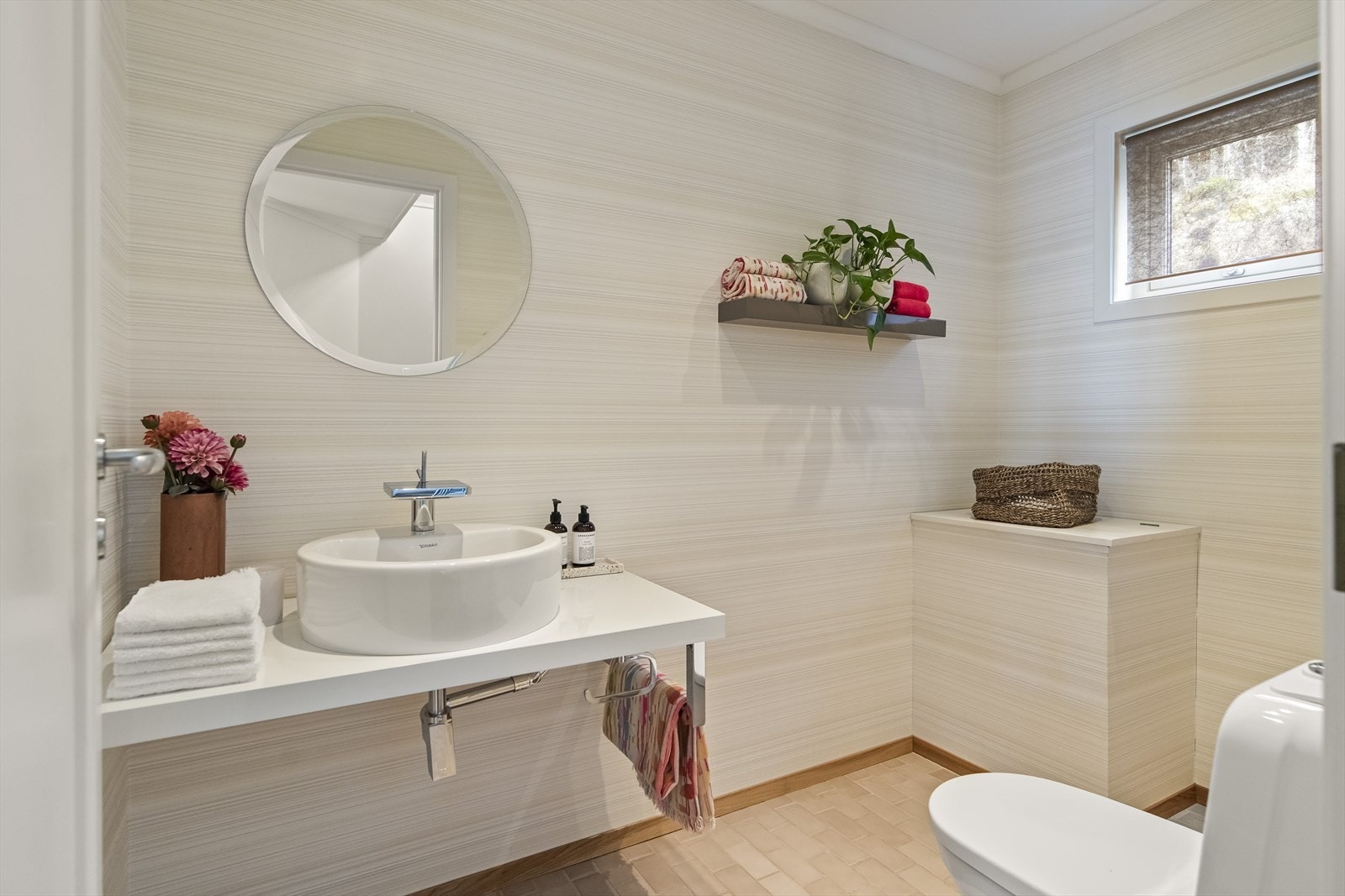 Wc-rommet er smakfullt innredet med lyse gulvfliser, downlights i taket og en delikat tapet på veggene. Utenom toalettet har rommet et rundt speil, en benk med toppmontert servant og en skittentøysjakt ned til vaskerommet. Galleribilde