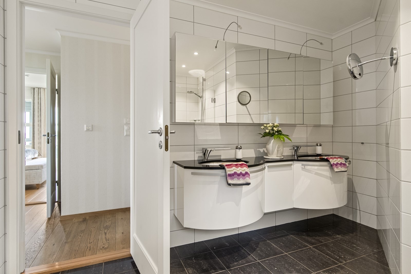 Varme er lagt i gulvet, og badet har downlights, vegghengt toalett og dagslys fra et lite vindu. Et stort speilskap med belysning er plassert over en stilig skuffeseksjon med hvite fronter og dobbel servant. Galleribilde