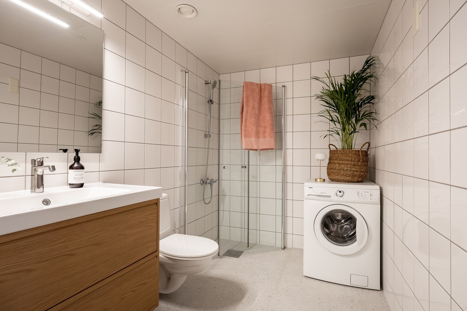 Romslig og delikat bad med moderne baderomsinnredning og vegghengt speil med integrert belysning. Dusjhjørne med innfellbare dusjvegger, vegghengt toalett og opplegg for vaskemaskin. Galleribilde