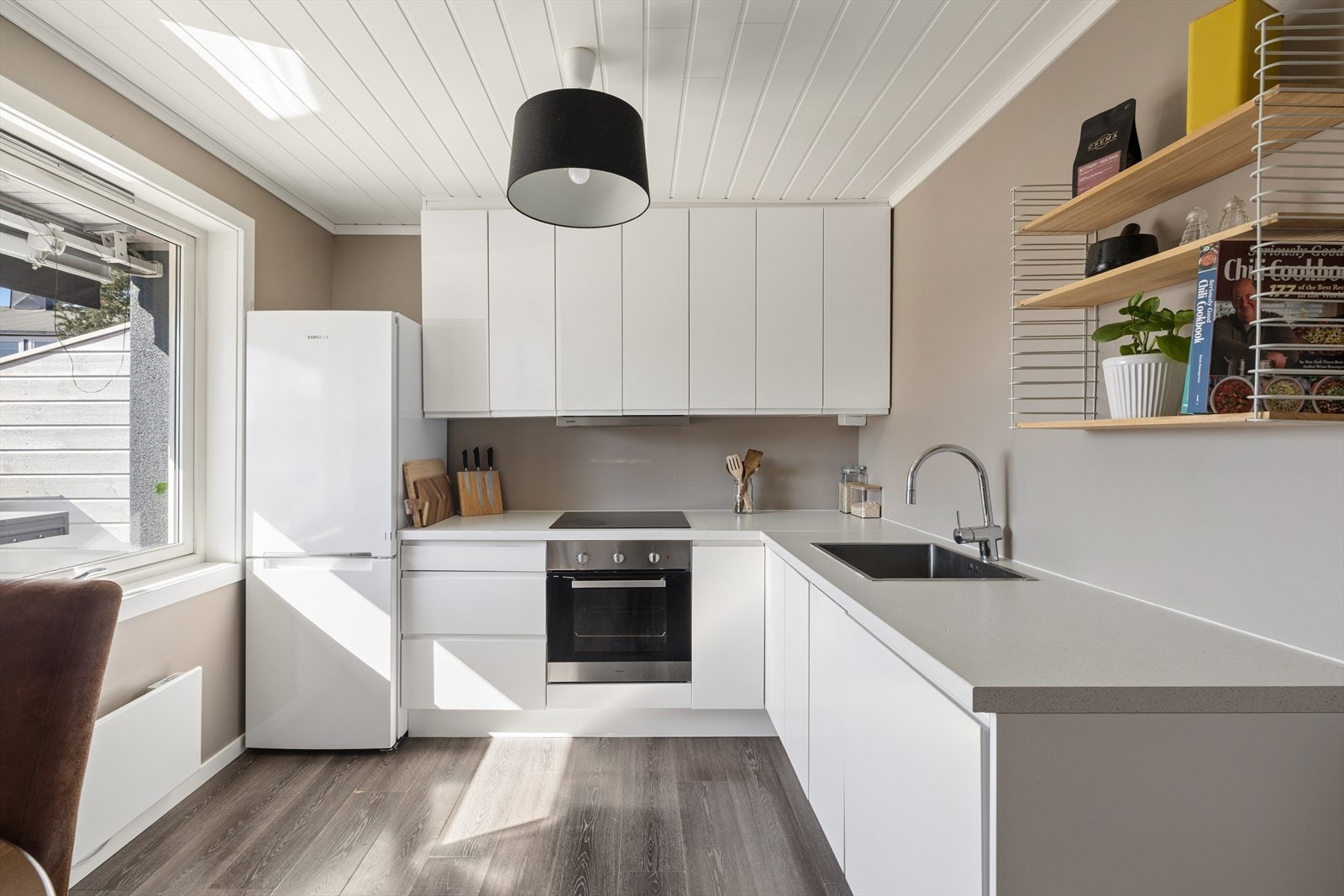 Kjøkkeninnredning med hvite glatte fronter. Malte flater over laminat benkeplate med nedfelt kum i rustfritt stål. Galleribilde