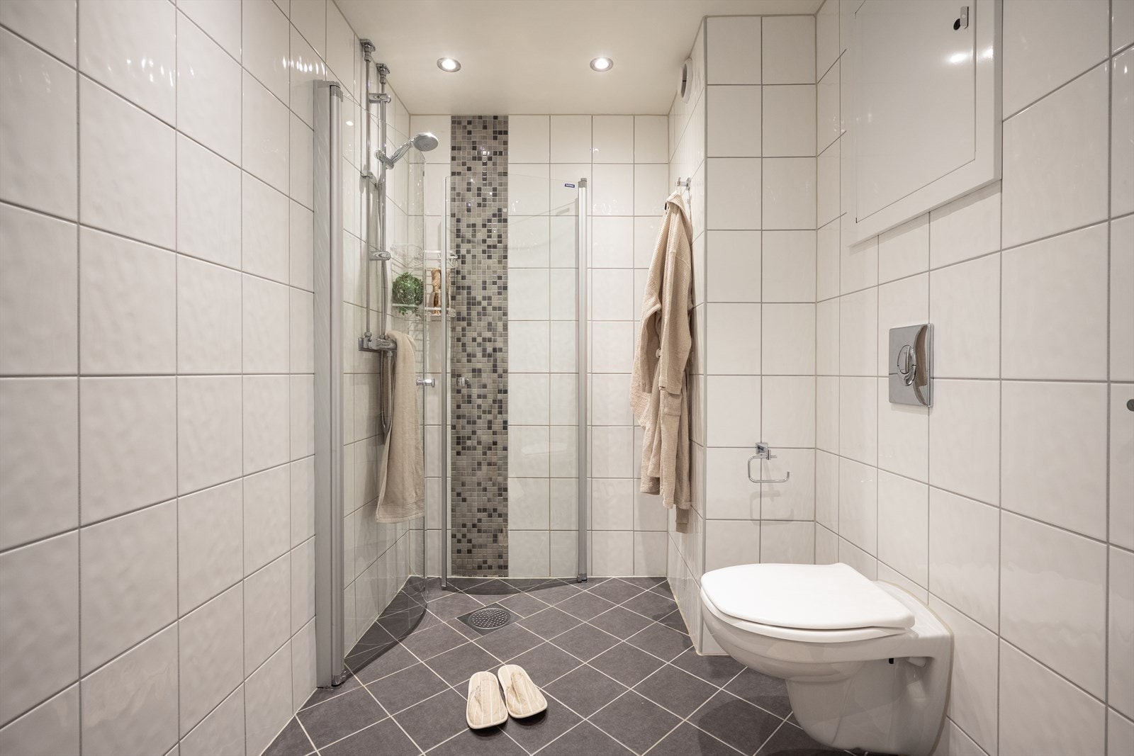 Himling med malte plater og innfelte downlights gir god belysning, mens flislagte vegger og gulv med vannbåren gulvvarme bidrar til et komfortabelt og praktisk rom. Galleribilde