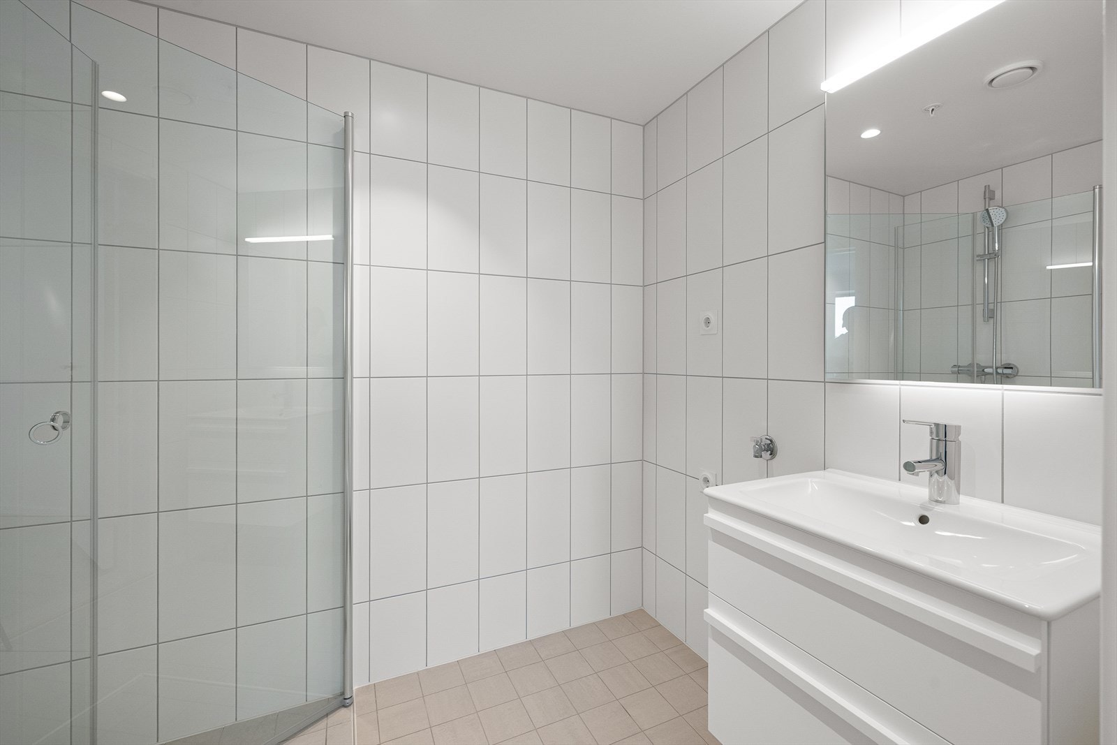 Badet inneholder servant med innredning, speil med lysarmatur, veggmontert toalett og dusjhjørne med dusjvegger i glass. Opplegg til vaskemaskin. Galleribilde