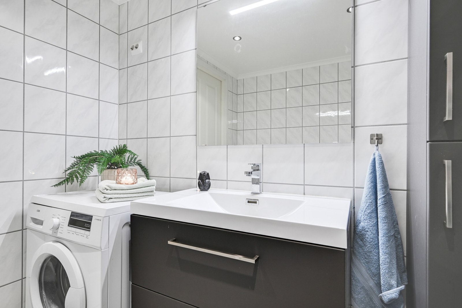 Badet inneholder servant med moderne innredning, speil, veggmontert wc, dusjhjørne og opplegg for vaskemaskin - praktisk og romslig løsning. Galleribilde