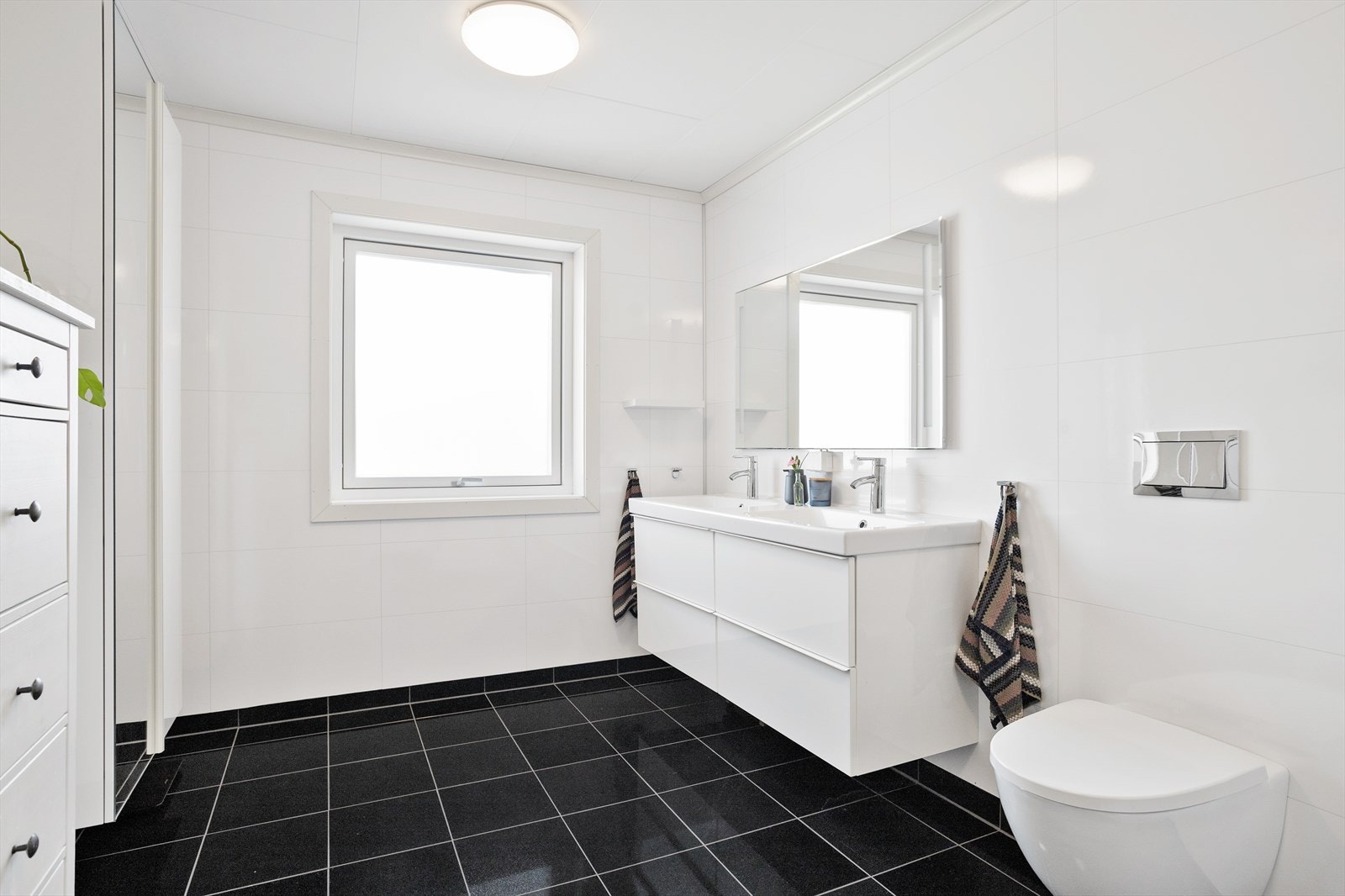 Badet er utstyrt med dusjkabinett, vegghengt toalett og et stilrent baderomsmøbel med doble servanter - en praktisk og etterspurt løsning som gjør morgenrutinene både enklere og mer komfortable for hele husstanden. Galleribilde