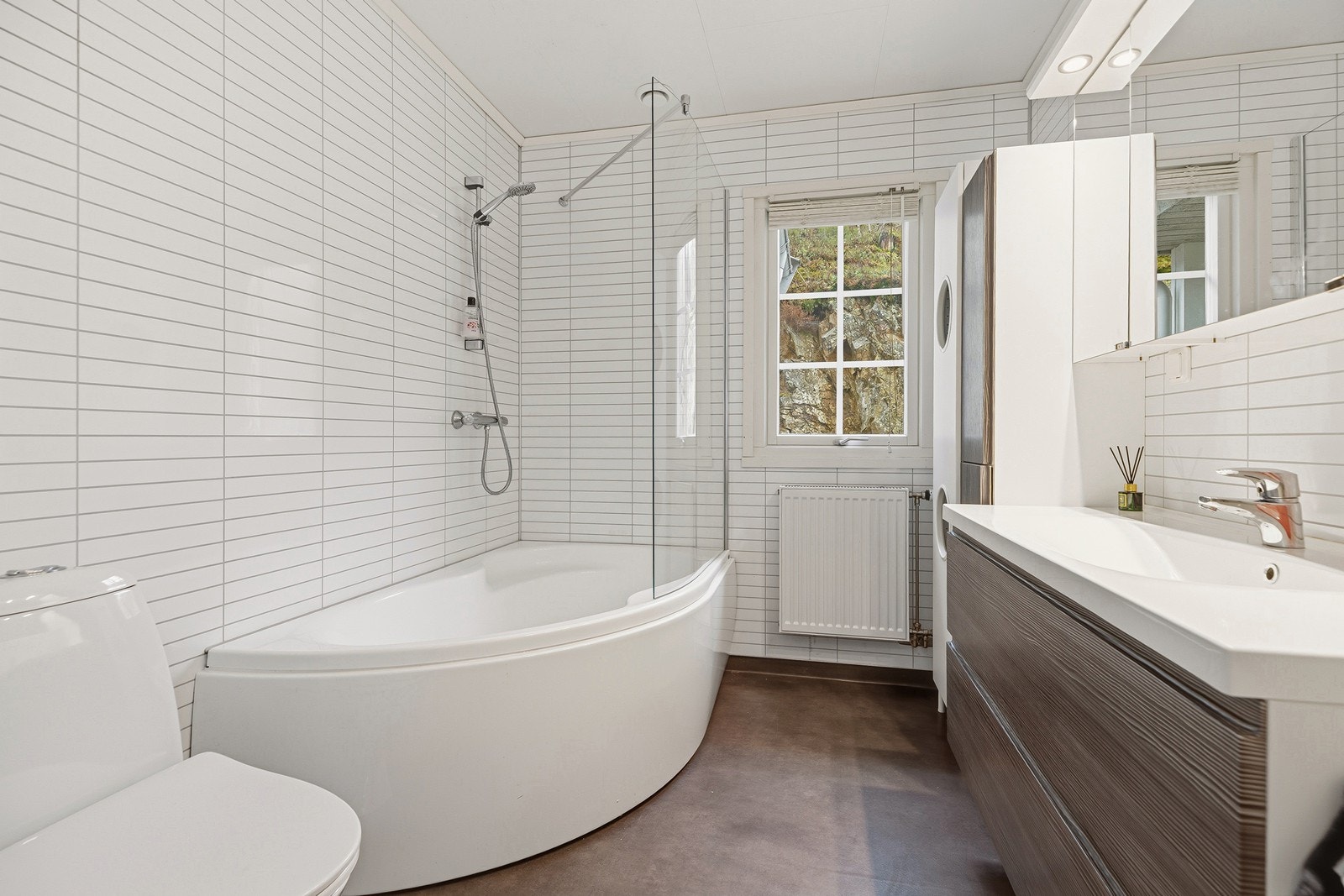 Pent bad med vinylbelegg på gulv og baderomsplater på vegger. Badet er innredet med nedfelt servant, toalett og badekar Galleribilde