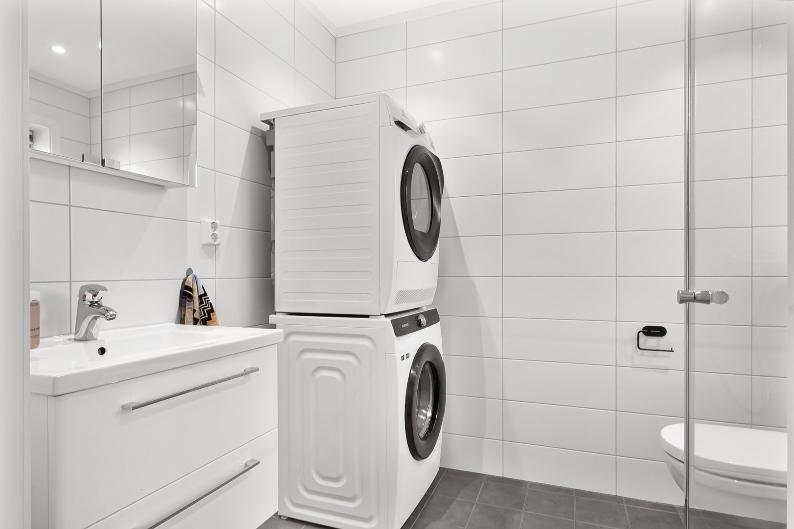 Badet i denne etasjen er kombinert med vaskerom og ligger rett ved inngangen - ideelt for småbarnsfamilier eller husets firbente. Rommet er innredet med servant med skuffer, speil, veggmontert toalett og dusjhjørne. Galleribilde