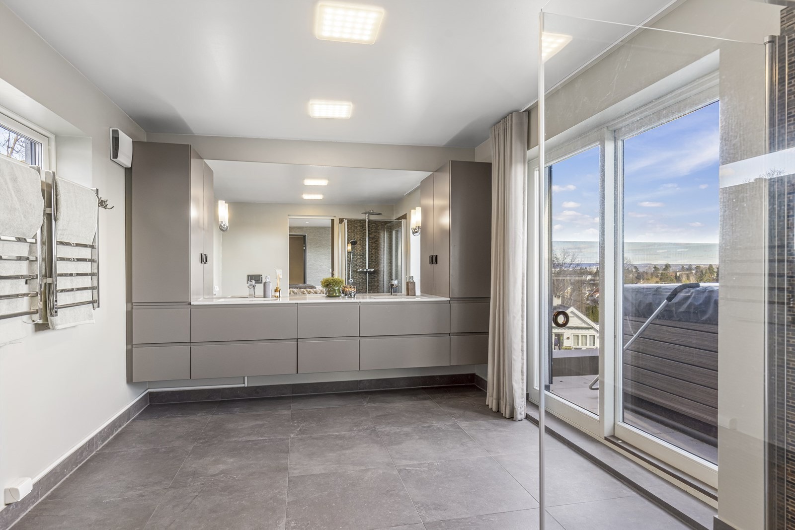Stort bad en-suite med dobbel servant, flislagt gulv med vannbåren varme og utgang til terrasse. Galleribilde
