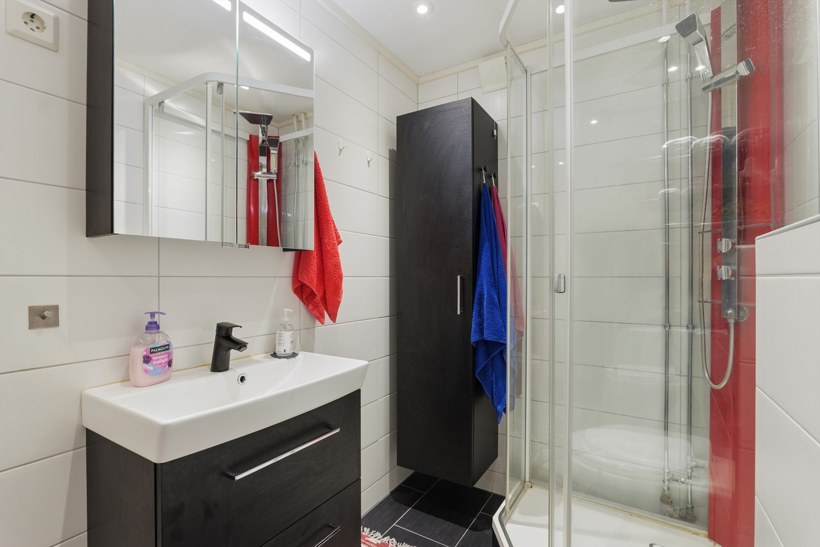 Badet fremstår som moderne og velholdt, med klassisk flislagte overflater i lyse fargetoner som gir et rent og tidløst uttrykk. Gulvet er belagt med mørke fliser som skaper fin kontrast og gir rommet et helhetlig preg. Galleribilde