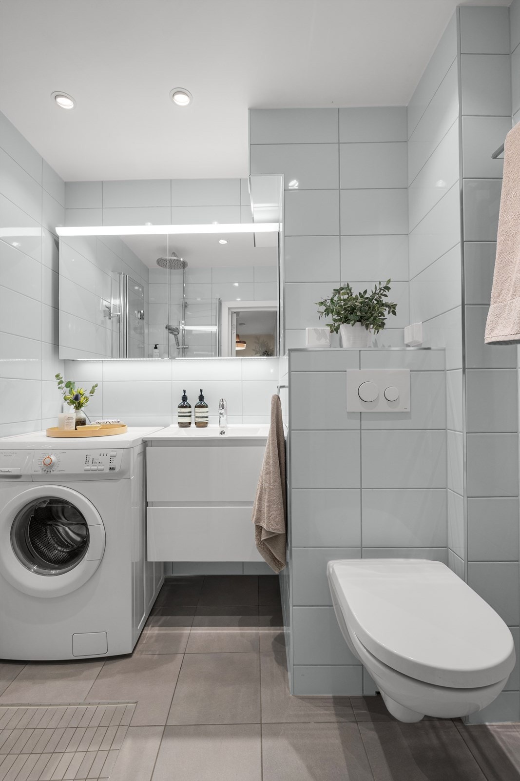 Baderomsinnredningen består av veggmonterte dusjdører, servant med underskap, speilskap med lys over, veggmontert wc og opplegg for vaskemaskin. Galleribilde
