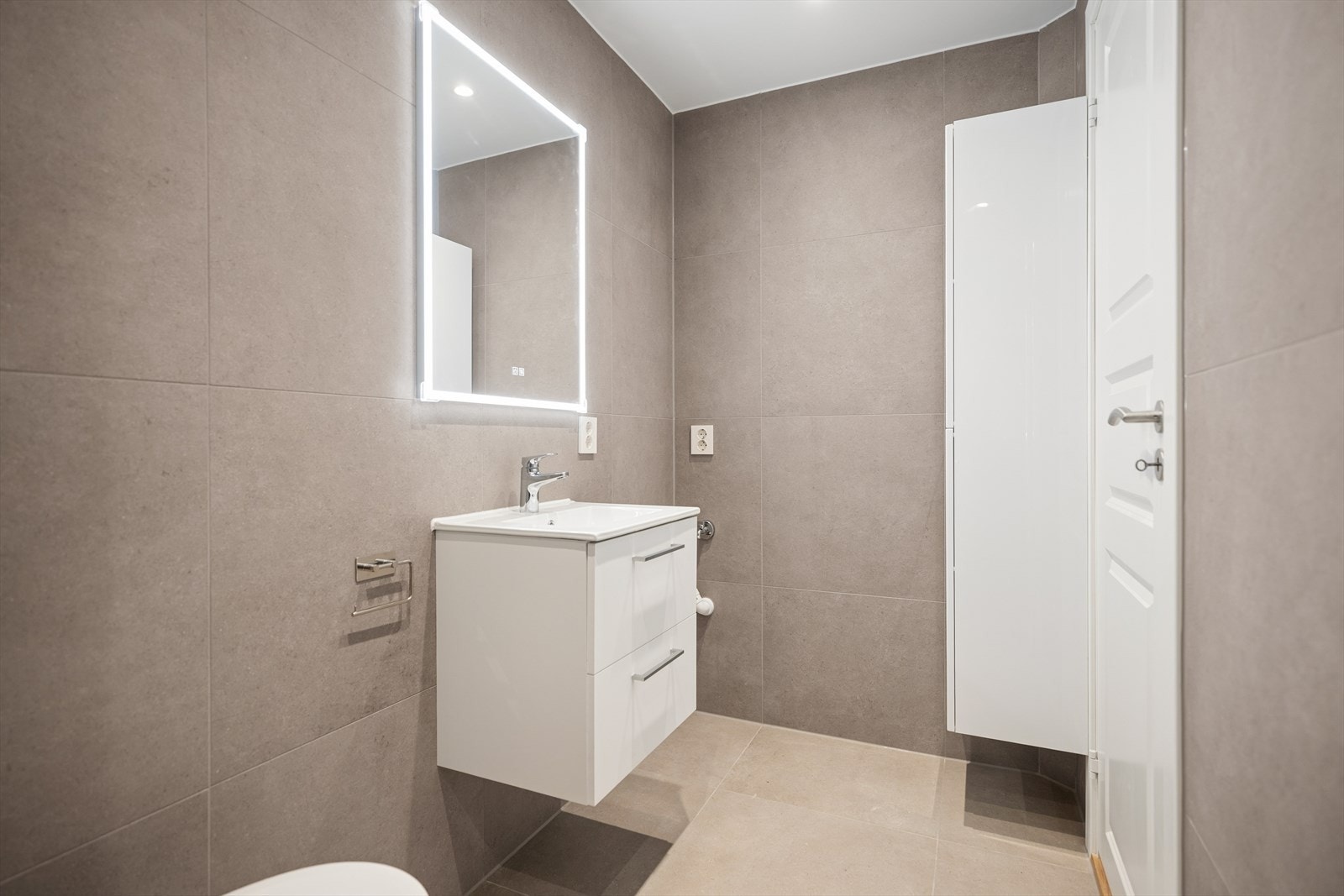 Badet sett fra dusjsonen. Servant med underskap, speil med belysning og baderomsdør. Varmekabler i gulv for ekstra komfort. Galleribilde