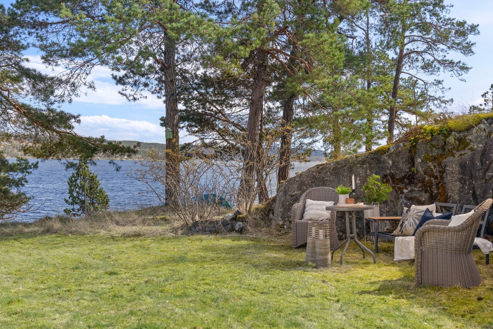 Koselig uteområde med sjøutsikt, omgitt av trær og gressplen. Galleribilde