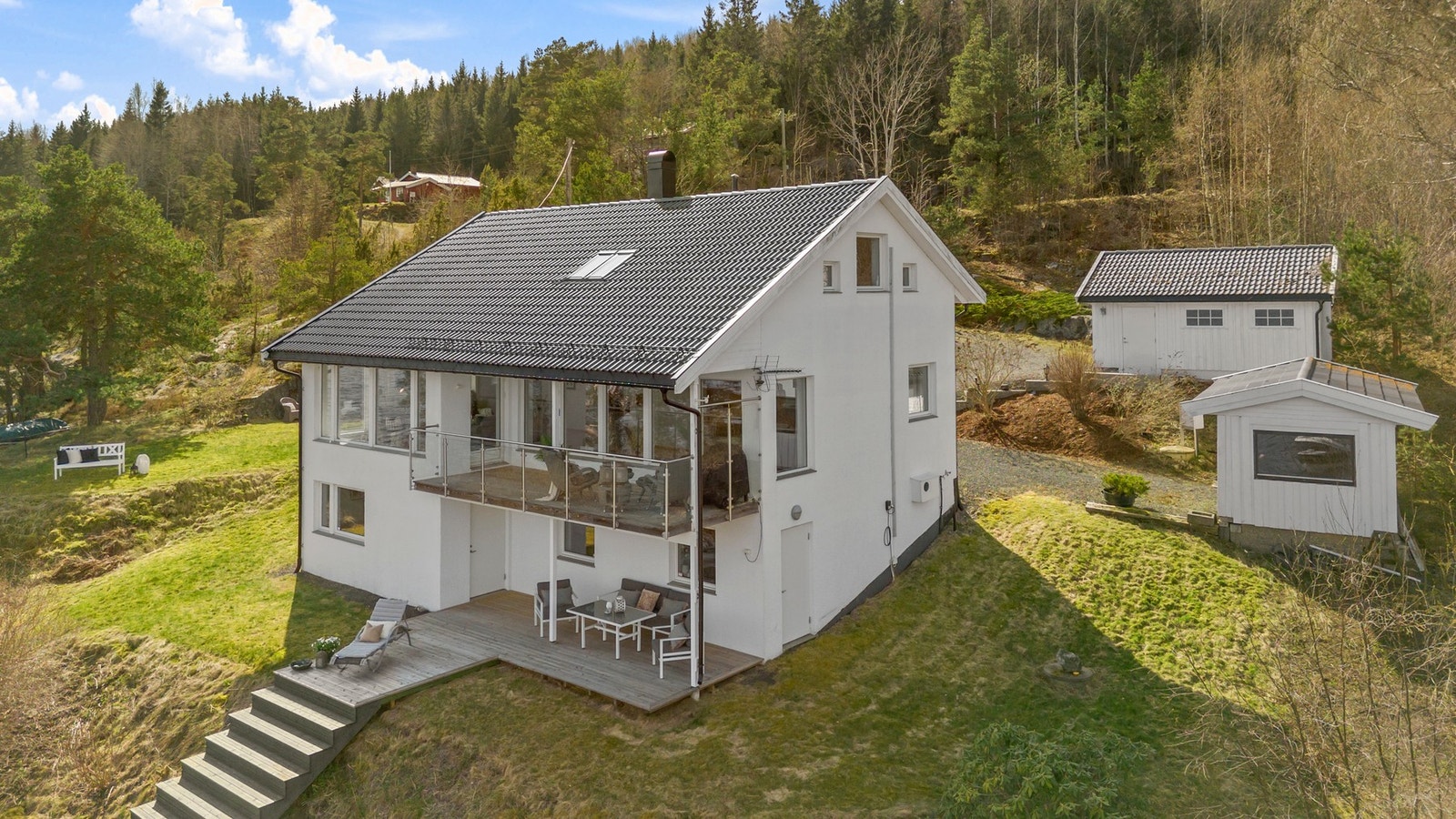 Enebolig med hvit fasade, stor balkong og bod og dobbel garasje, omgitt av fjord og skogkledd natur. Galleribilde