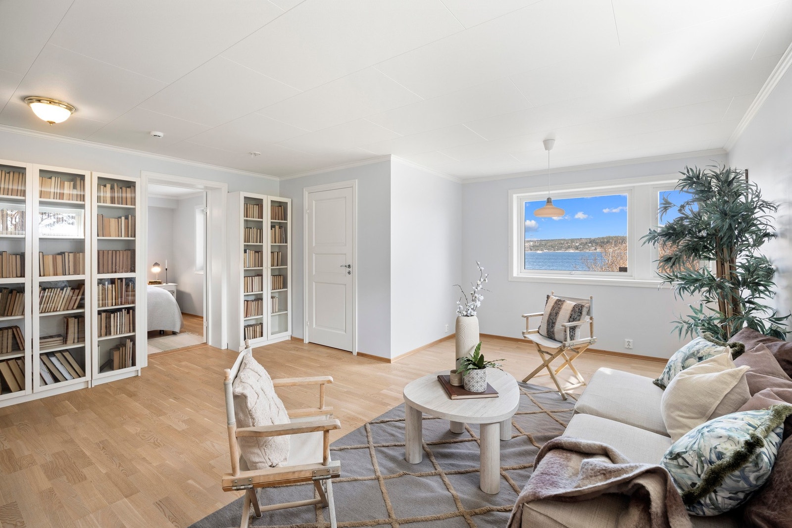 Lys stue med store vinduer og utsikt mot vannet. Rommet har god plass til både sittegruppe og bokhyller. Galleribilde