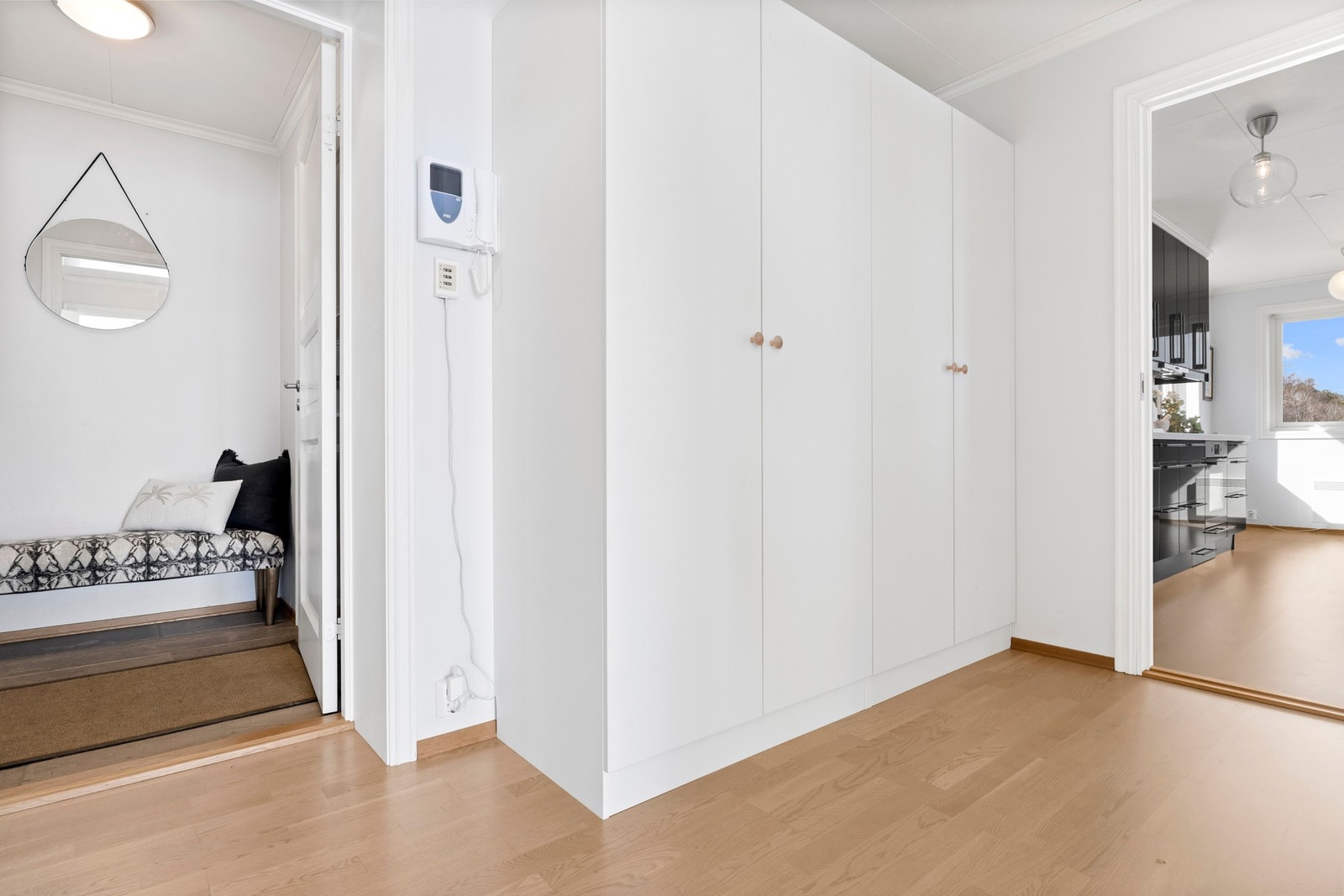 Lys gang med garderobeskap og tilgang til kjøkken og et annet rom. Galleribilde