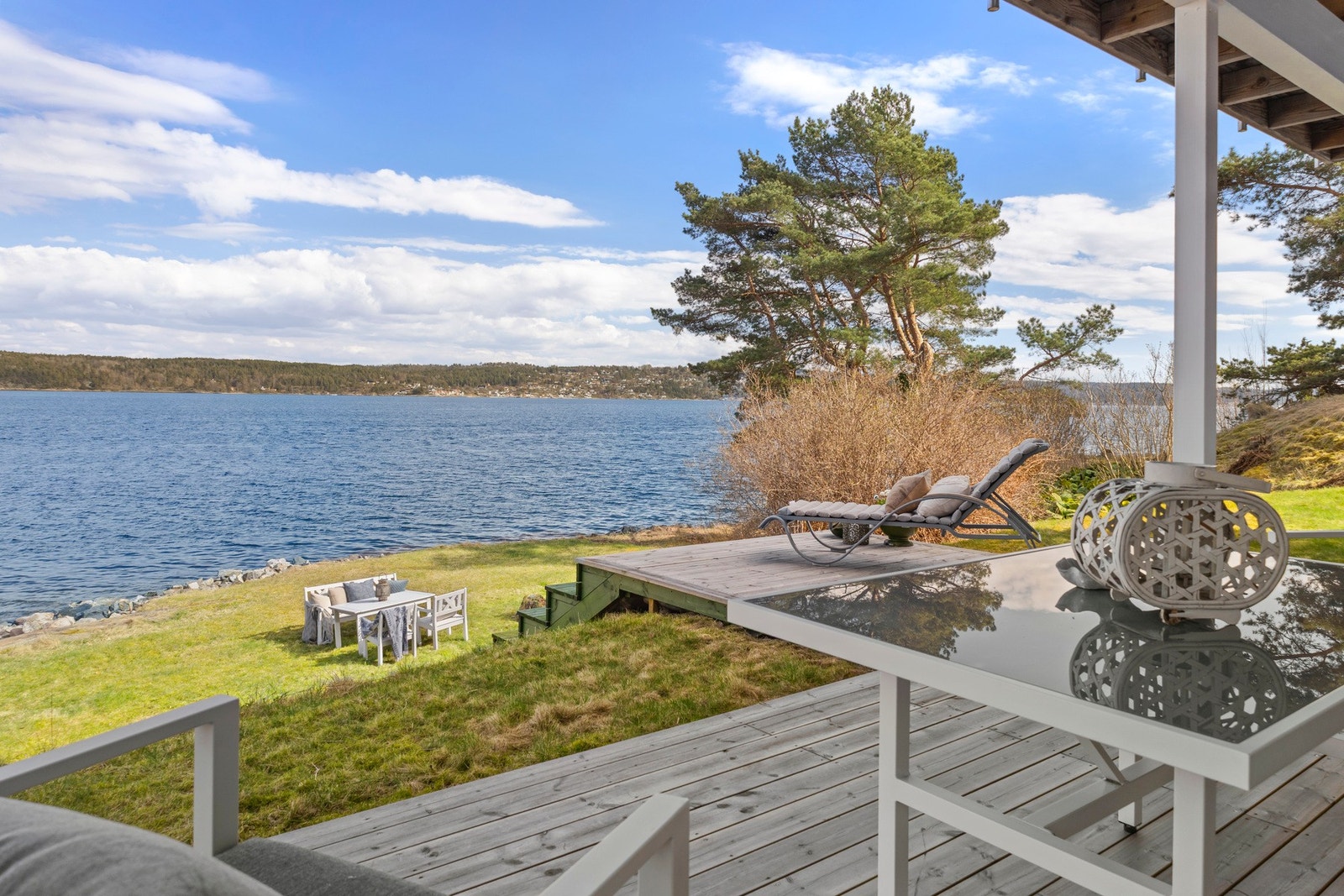 Utsikt mot sjøen fra terrasse med gressplen og trær i bakgrunnen. Galleribilde