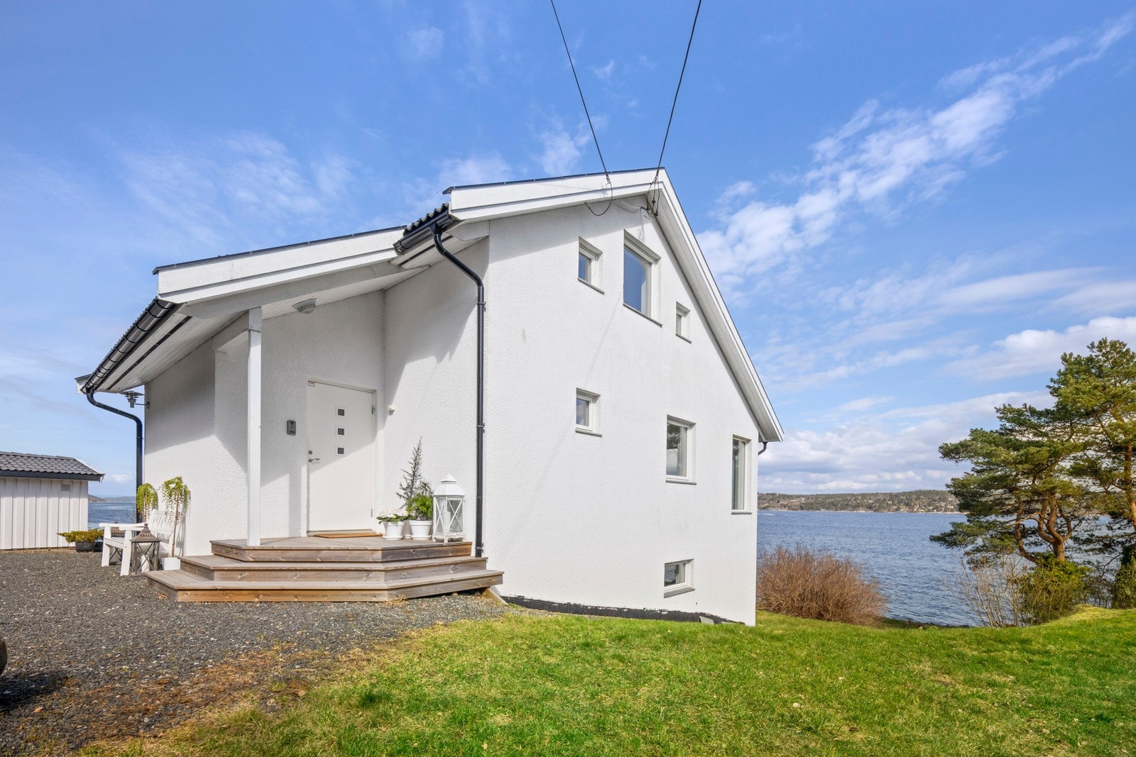 Hvit enebolig med skråtak, beliggende ved vannet, med utsikt over sjøen. Galleribilde