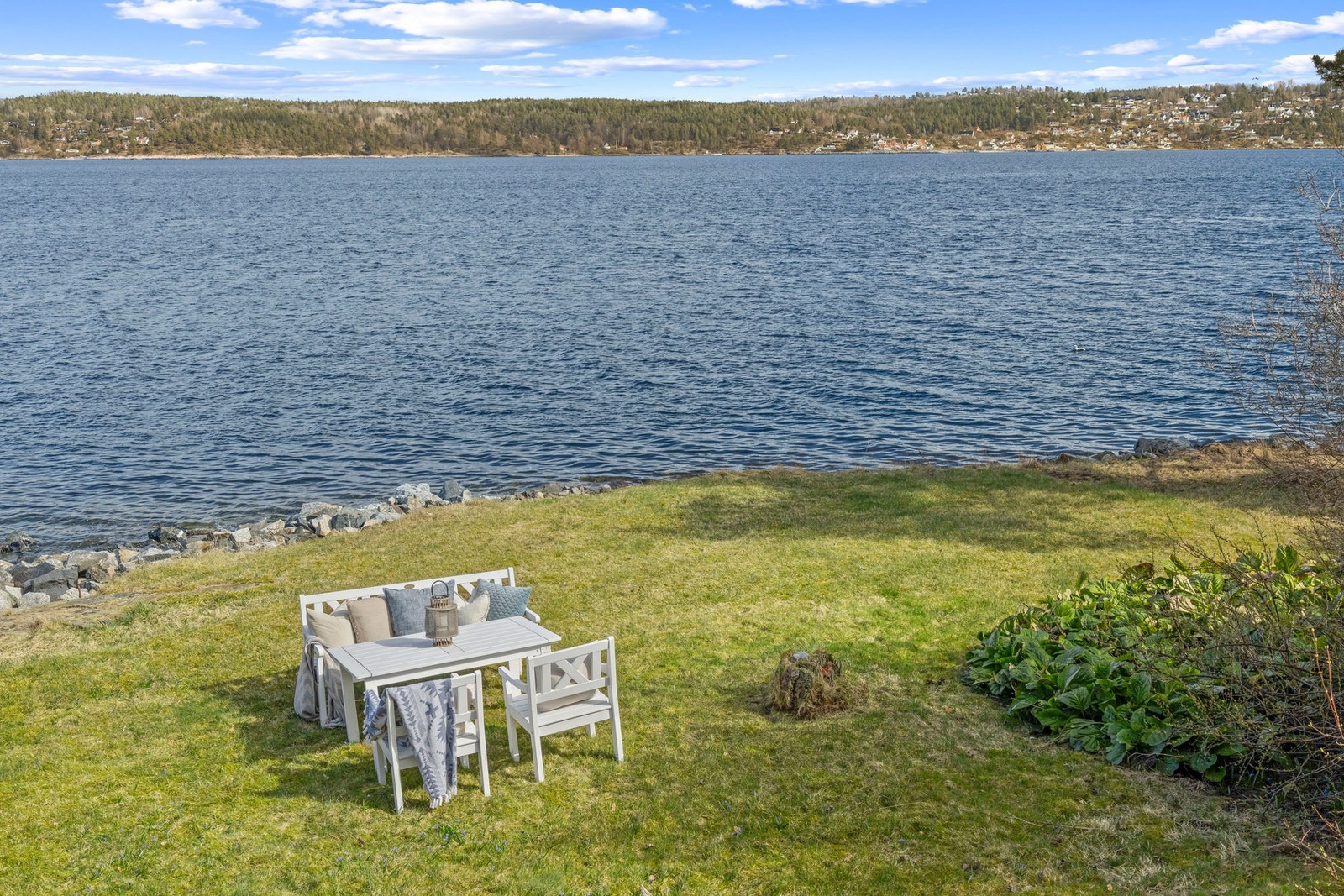 Utsikt mot vannet med gressplen og steinmur langs vannkanten. Galleribilde
