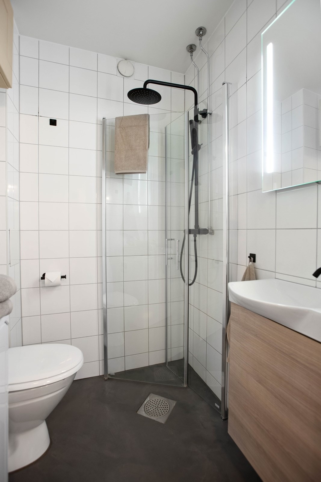 Badet er innredet med servant med underskap, speil med sidelys, frittstående toalett, dusjhjørne med svingbare glassdører og opplegg for vaskemaskin. Galleribilde