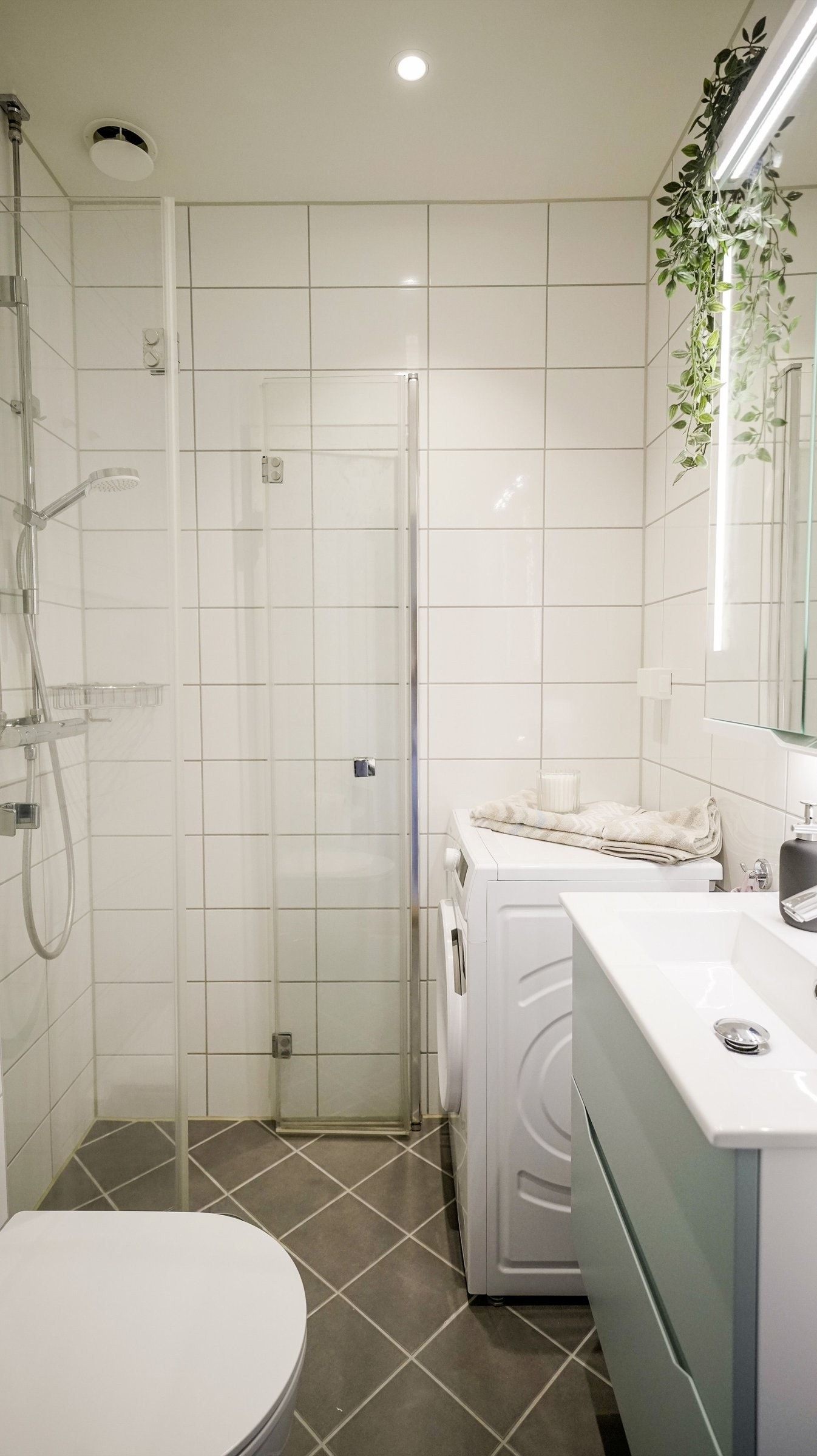 Badet består av dusjhjørne, vegghengt toalett, opplegg for vaskemaskin og servant med to skuffer og ett-greps blandebatteri. Galleribilde