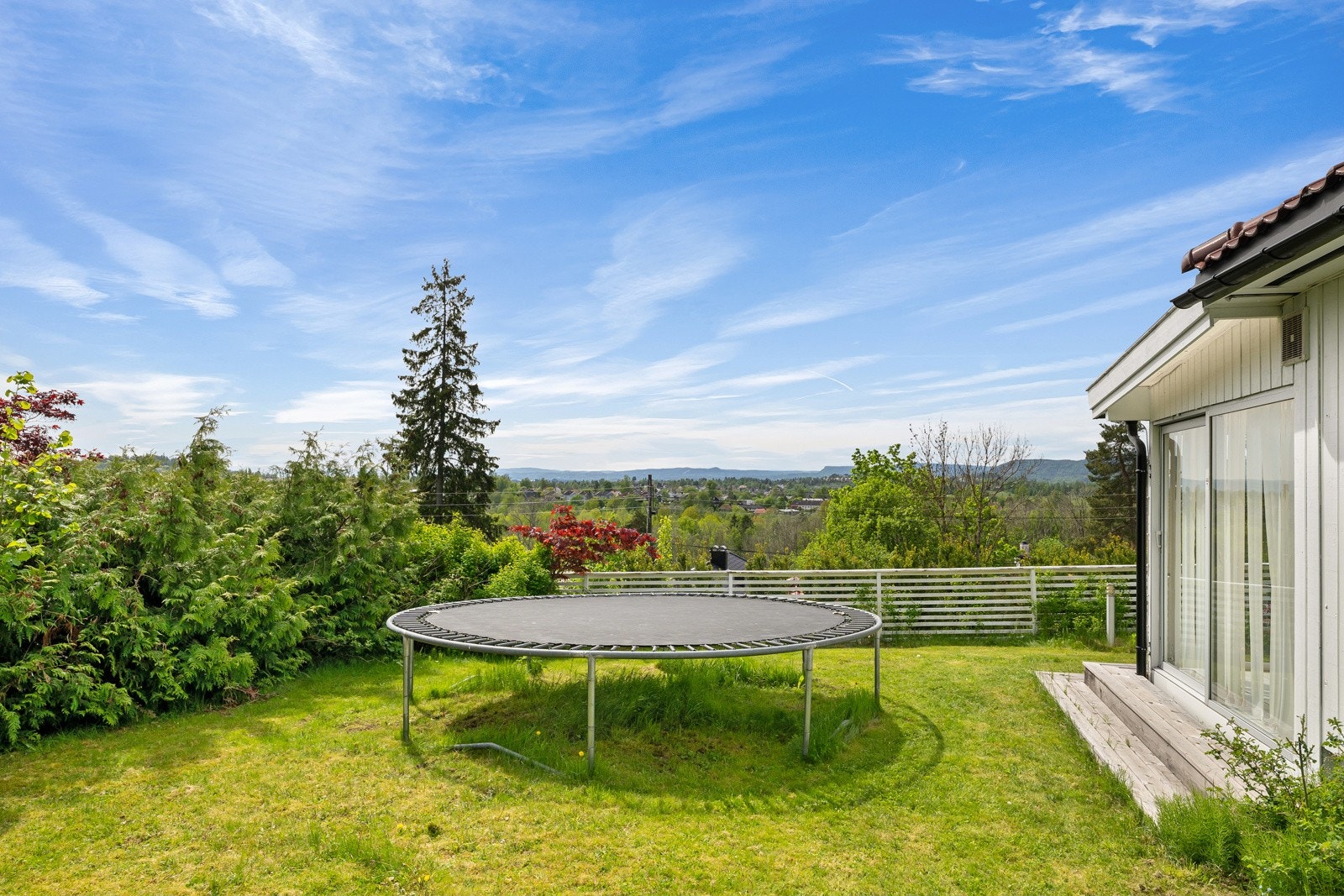 Tomten er omkranset av både plenarealer, naturtomt, busker og beplantning, og gir en fin kombinasjon av skjerming, lekearealer og soner med sol. Galleribilde