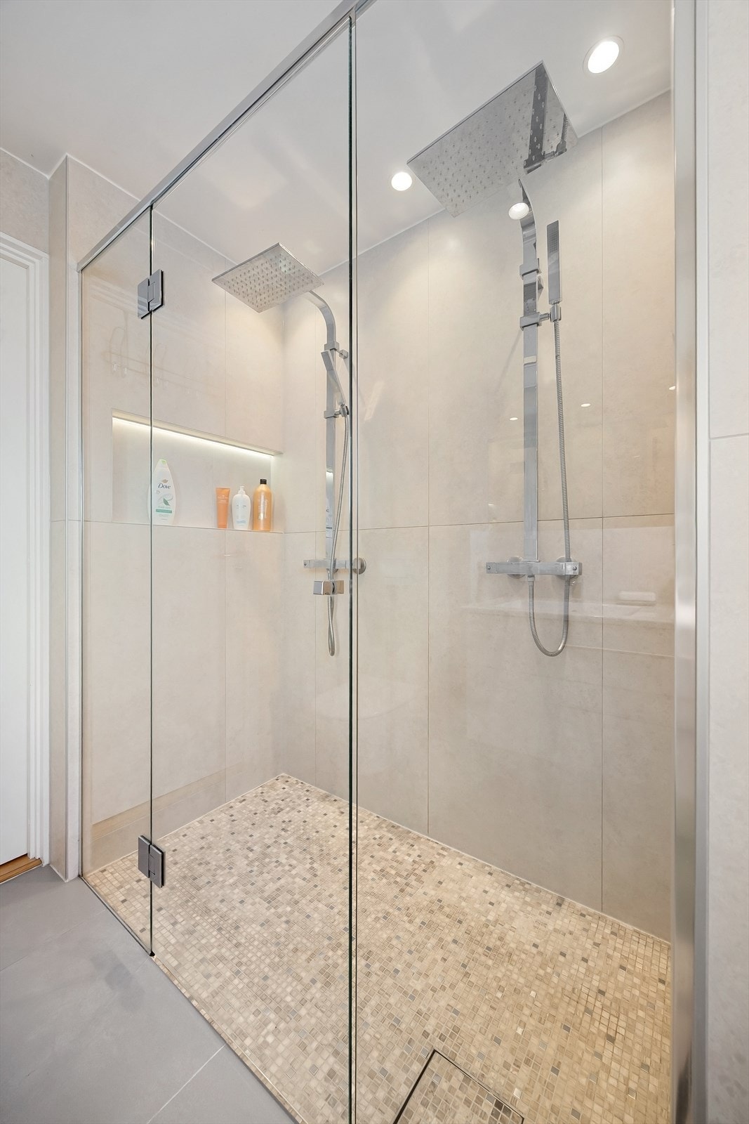 Badet har i tillegg en dobbel regnfallsdusj med mosaikkfliser på gulv Galleribilde