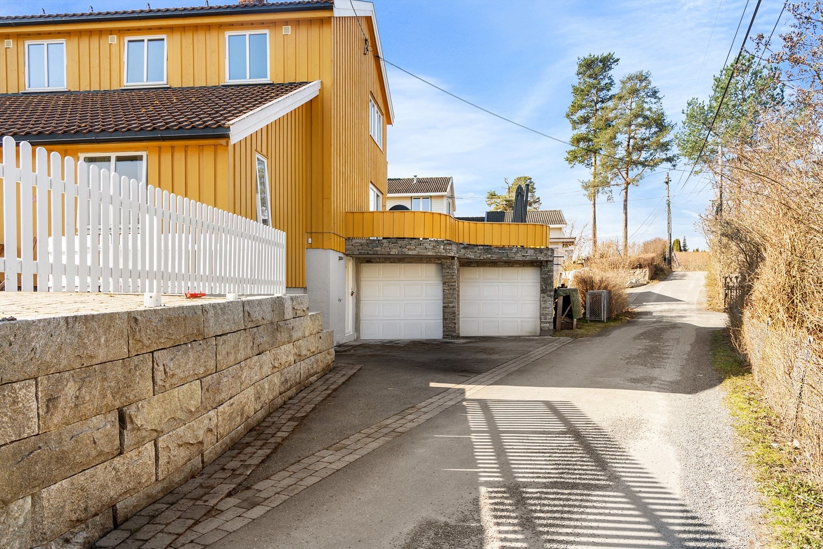 Tilhørende boligen er en dobbeltgarasje som ligger under verandaen. Herfra kan man gå opp til inngangspartiet via trapp eller direkte inn til boligen gjennom vaskerommet. Galleribilde