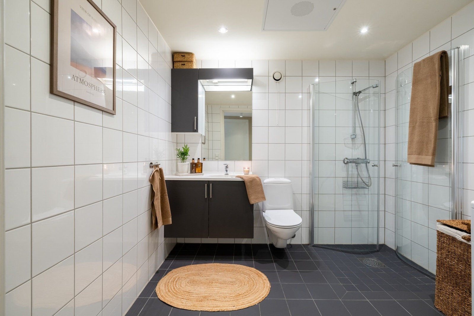 Baderommet har flislagt gulv og vegger og er av god størrelse. Badet er utstyrt med innredning med servant, vegghengt toalett og dusjhjørne med innfellbare dører. Galleribilde