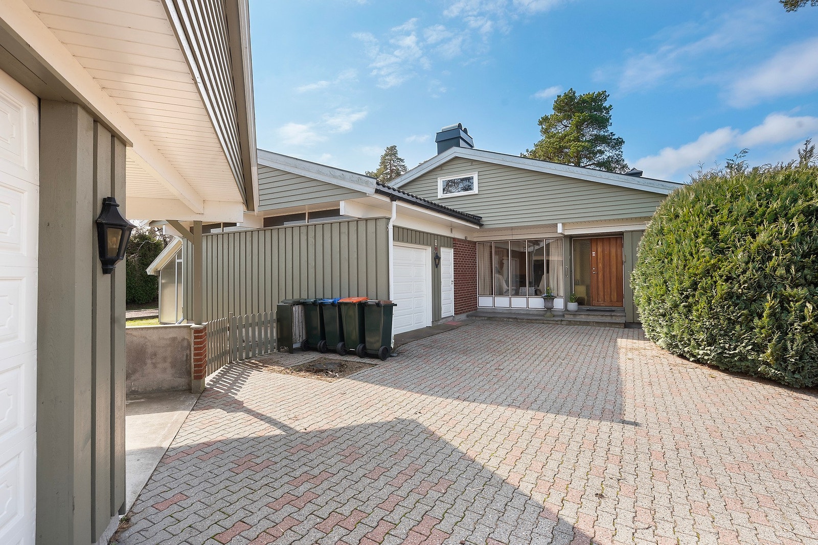 Ryddig gårdsplass med belegningsstein. En fritsående garasje med carport og en garasje i huset. Galleribilde