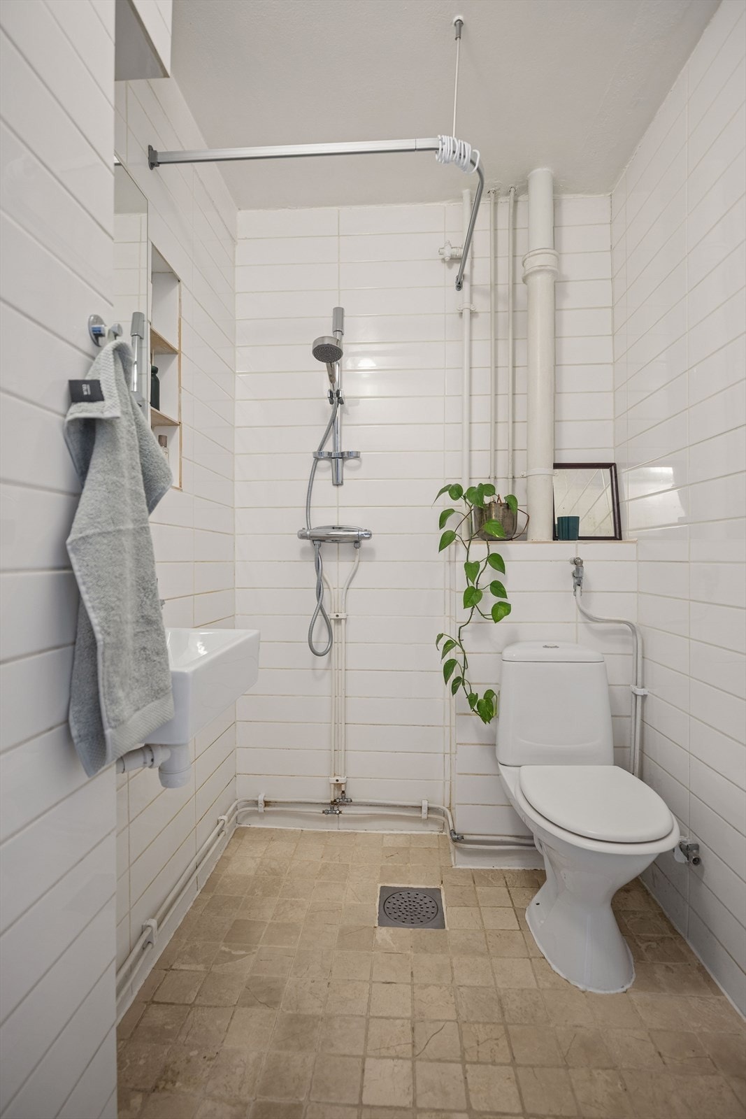 Badet fotografert fra døren viser åpen dusj uten kabinett og gulvsluk i steinheller. Galleribilde