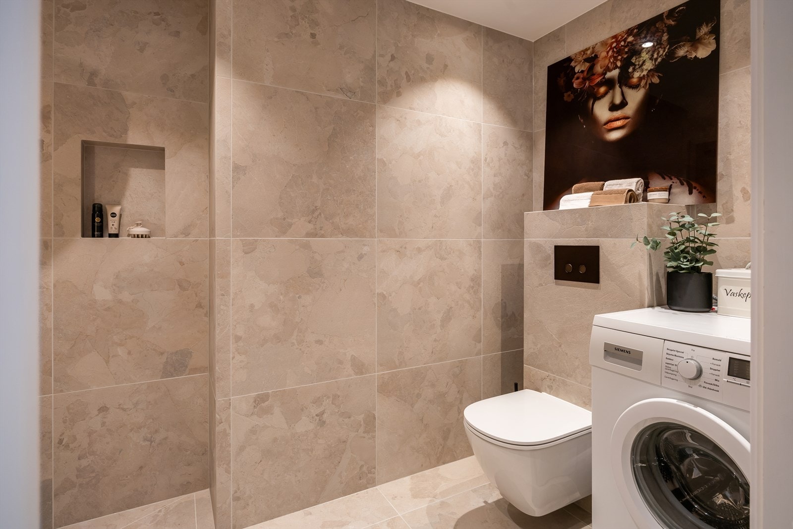 Badet er utstyrt med vegghengt toalett, innredning med servant, åpen dusjsone og opplegg for vaskemaskin. Galleribilde