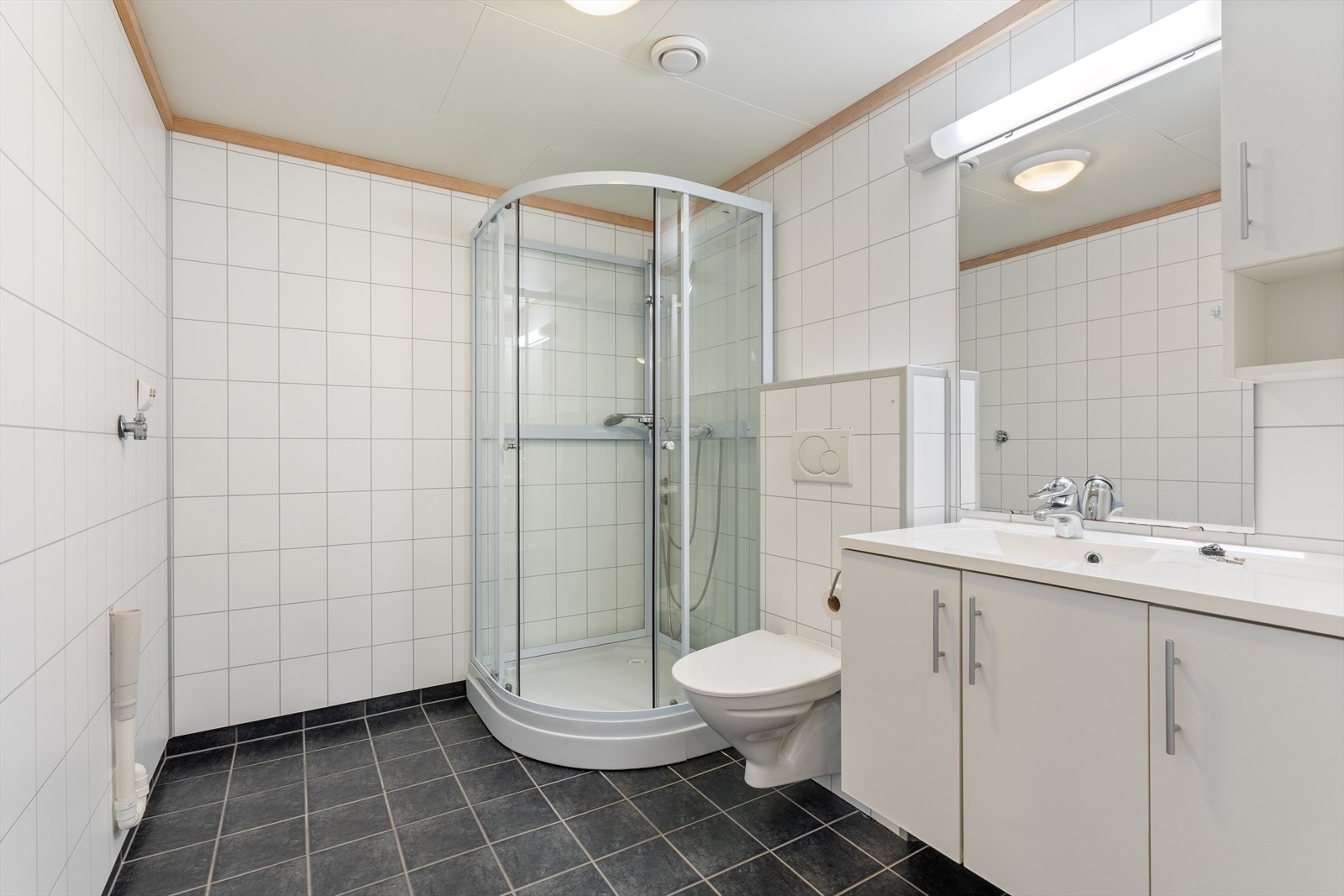 Bad/wc med fliser på gulv, varmekabler, opplegg for vaskemaskin, vegghengt toalett og dusjkabinett Galleribilde
