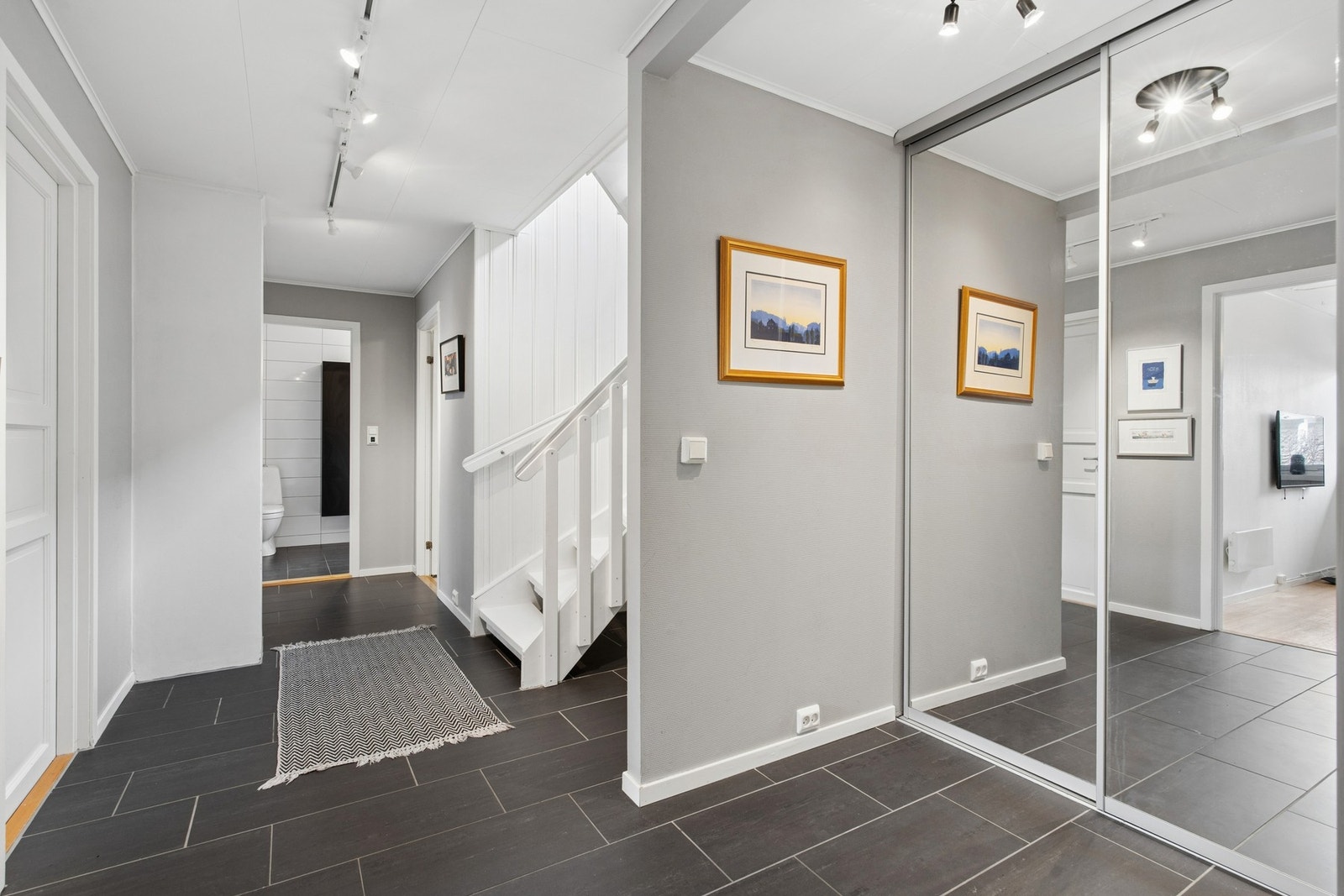 Romslig og innbydende hall med flislagt gulv og elegant trapperom som gir et solid førsteinntrykk av boligen. Galleribilde