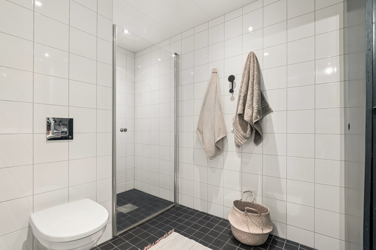 Baderommet har en tidløs utførelse, utstyrt med vegghengt toalett, dusjhjørne, servant med baderomsinnredning og speil, samt opplegg for vaskemaskin. Galleribilde
