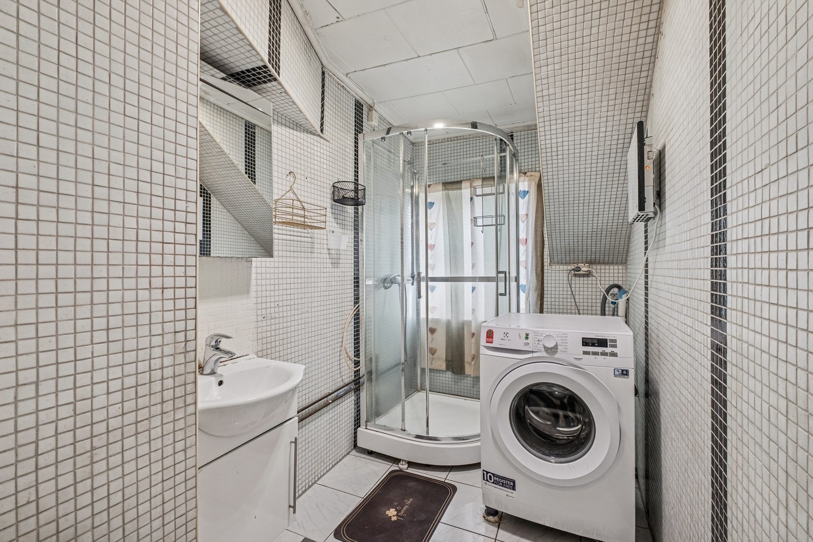 Badet er flislagt, utstyrt med dusjkabinett, baderomsinnredning med servant og har opplegg for vaskemaskin. Galleribilde