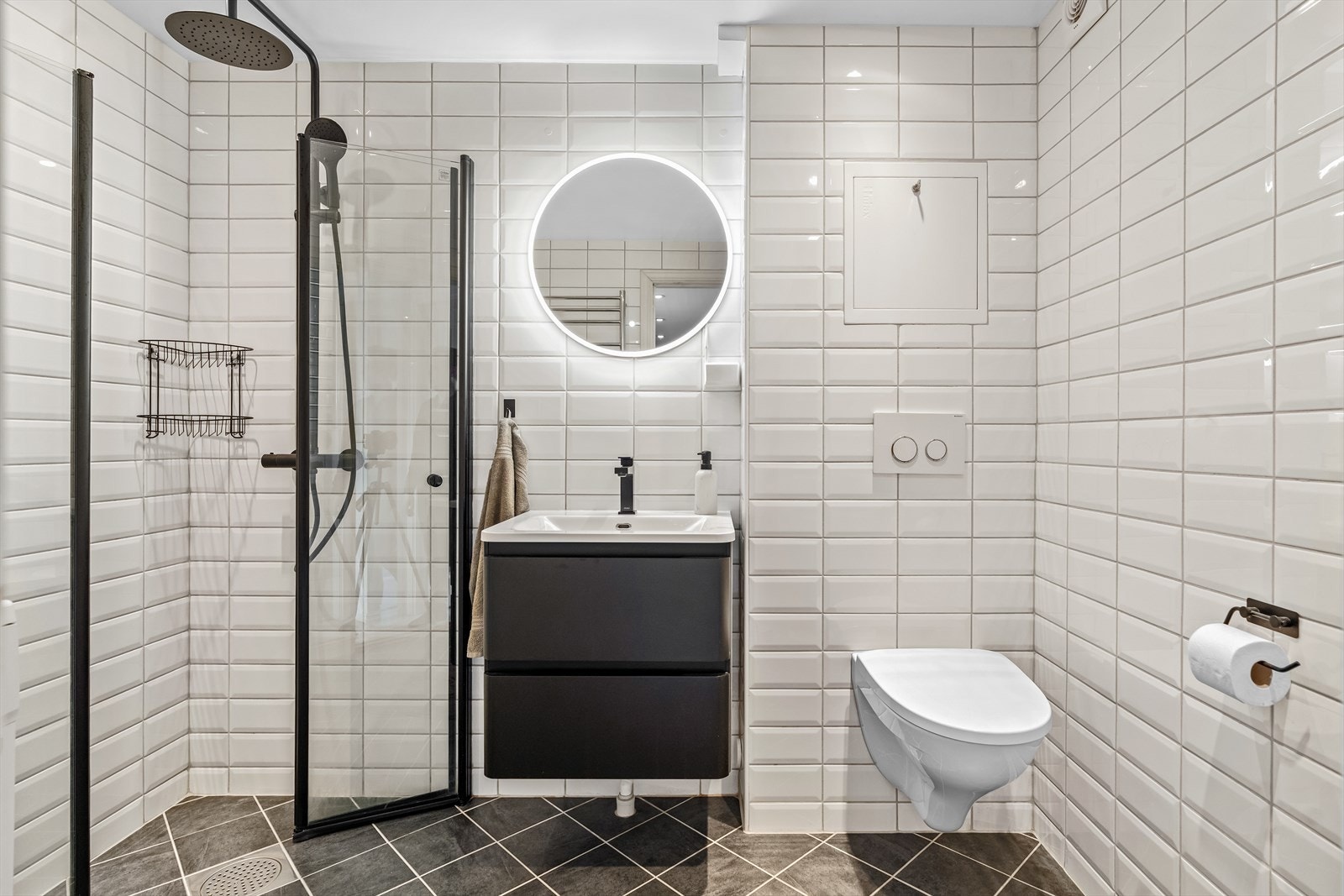 Badet har hvite fliser på vegger, mørke fliser på gulv, gulvvarme og downlights. Galleribilde