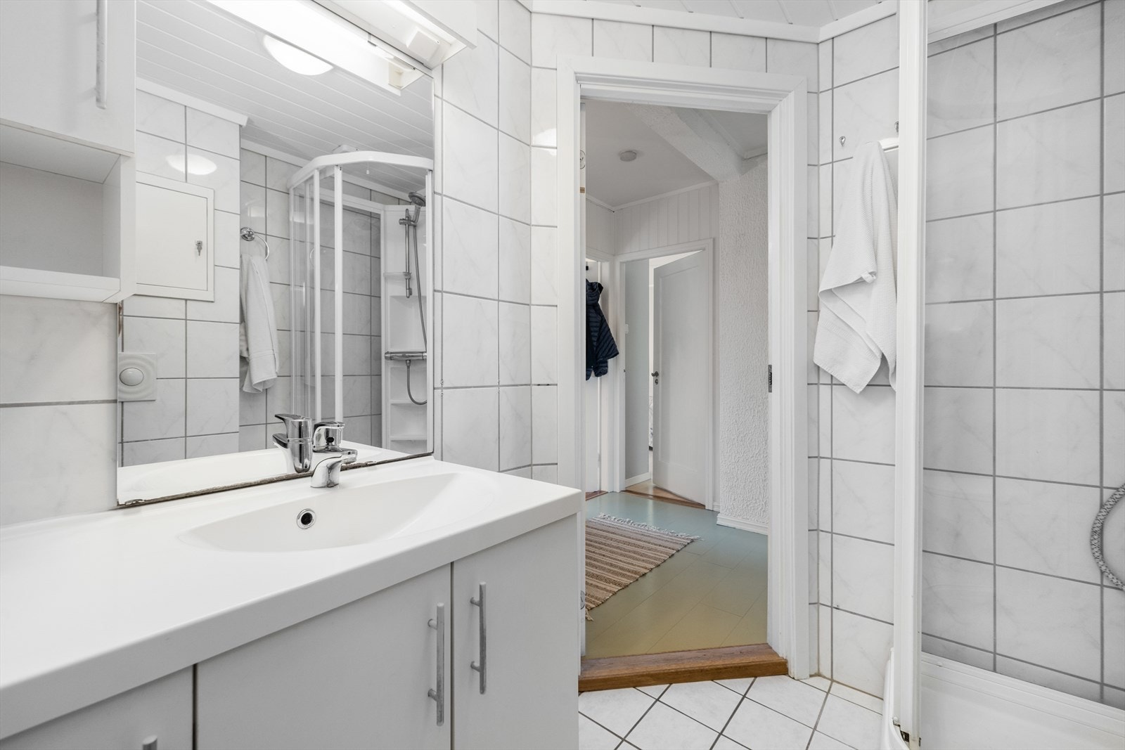 På badet er det slett hvit innredning med skapplass og heldekkende servant. Over innredningen er det vegghengskap og speilflate med lys over. Galleribilde