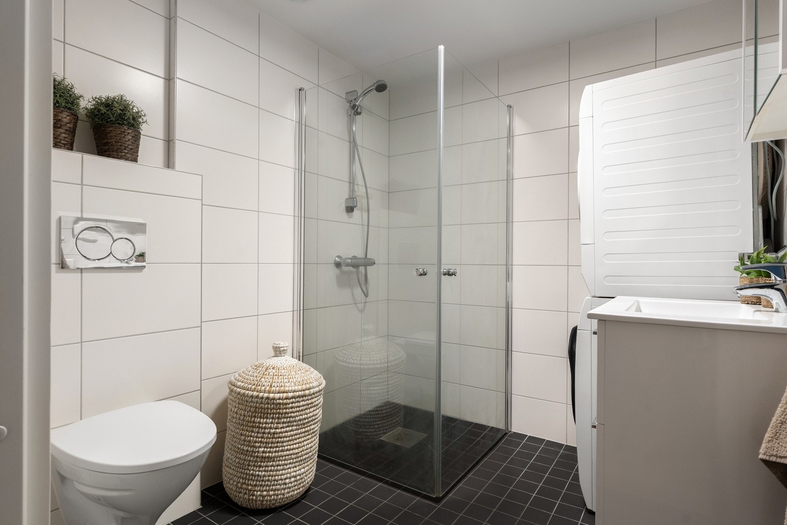 Innbydende baderom utstyrt med vegghengt toalett, dusj med glassdører og servant med tilhørende skuffer og speilskap