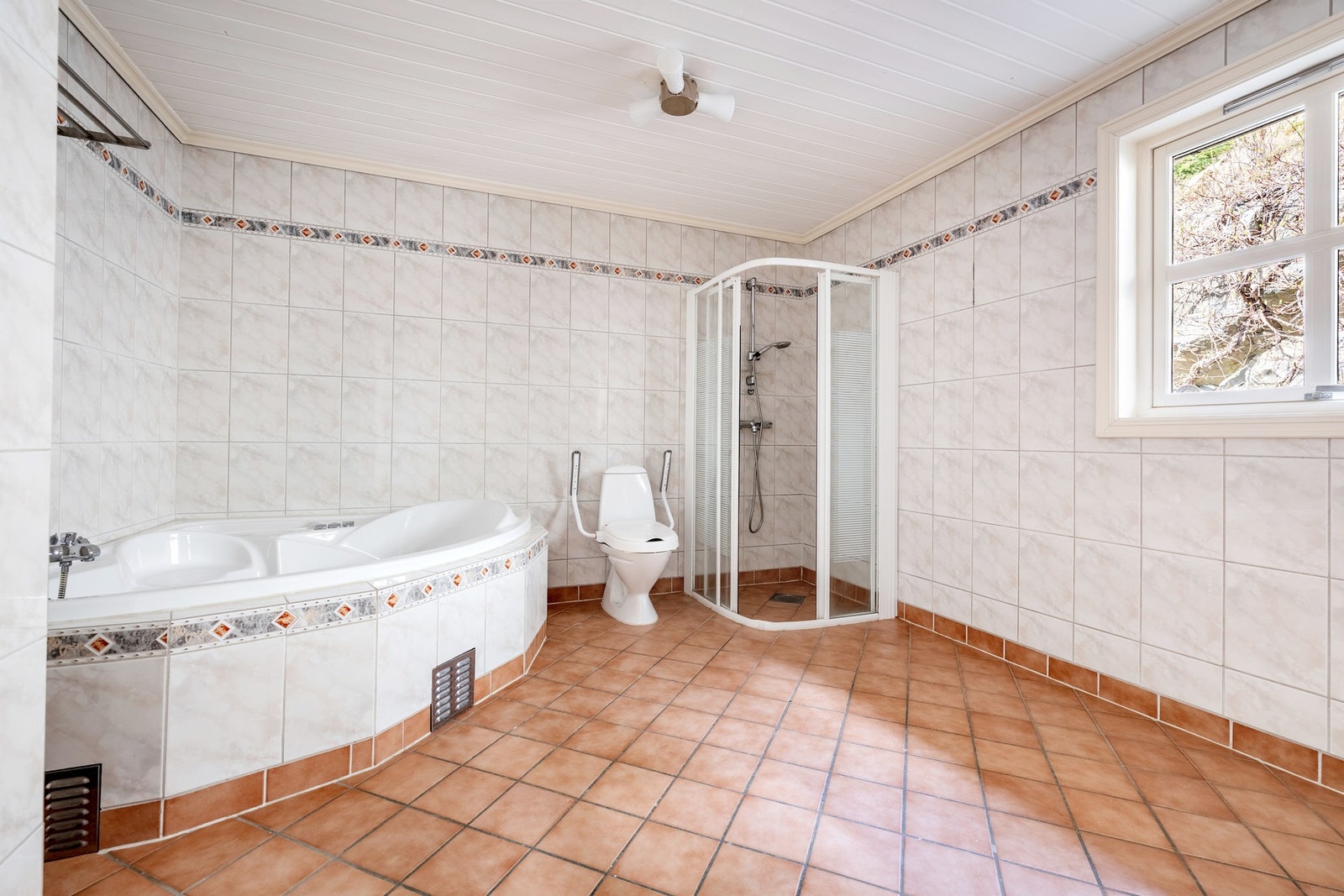 Badet er innredet med heldekkende flislagt plate med dobbel servant, speil på vegg over servant, gulvstående toalett, innfliset badekar og dusjnisje. Galleribilde