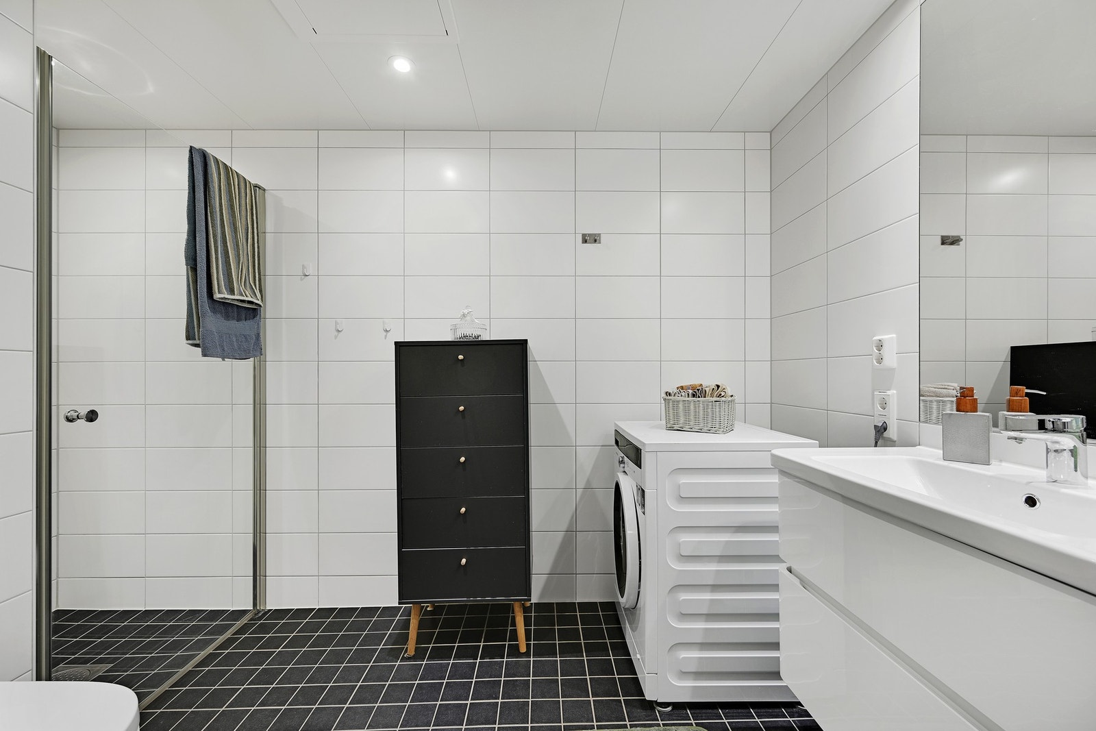 Badet inneholder servant med baderomsinnredning, veggmontert toalett, dusjhjørne med glassdør og opplegg for vaskemaskin. Galleribilde