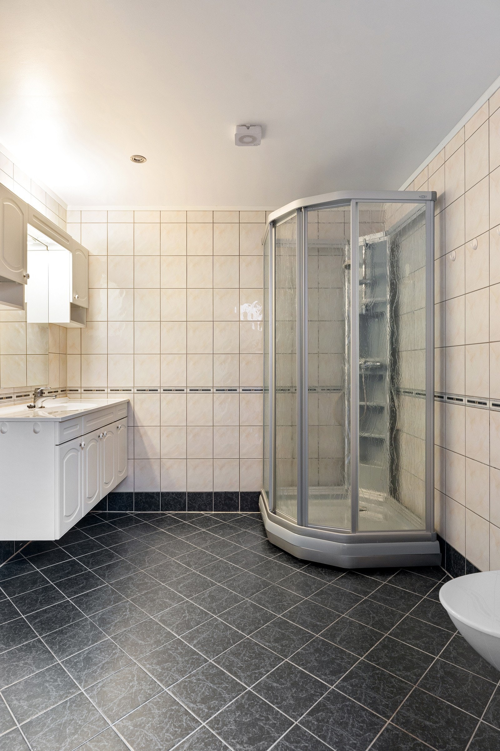 Stort flislagt bad med dusjkabinett og stor innredning for oppbevaring av baderomsartikler.