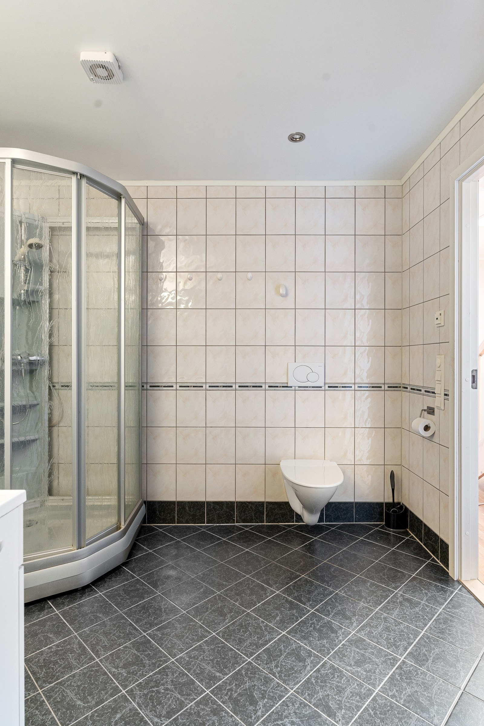 Stort flislagt bad med dusjkabinett og stor innredning for oppbevaring av baderomsartikler.