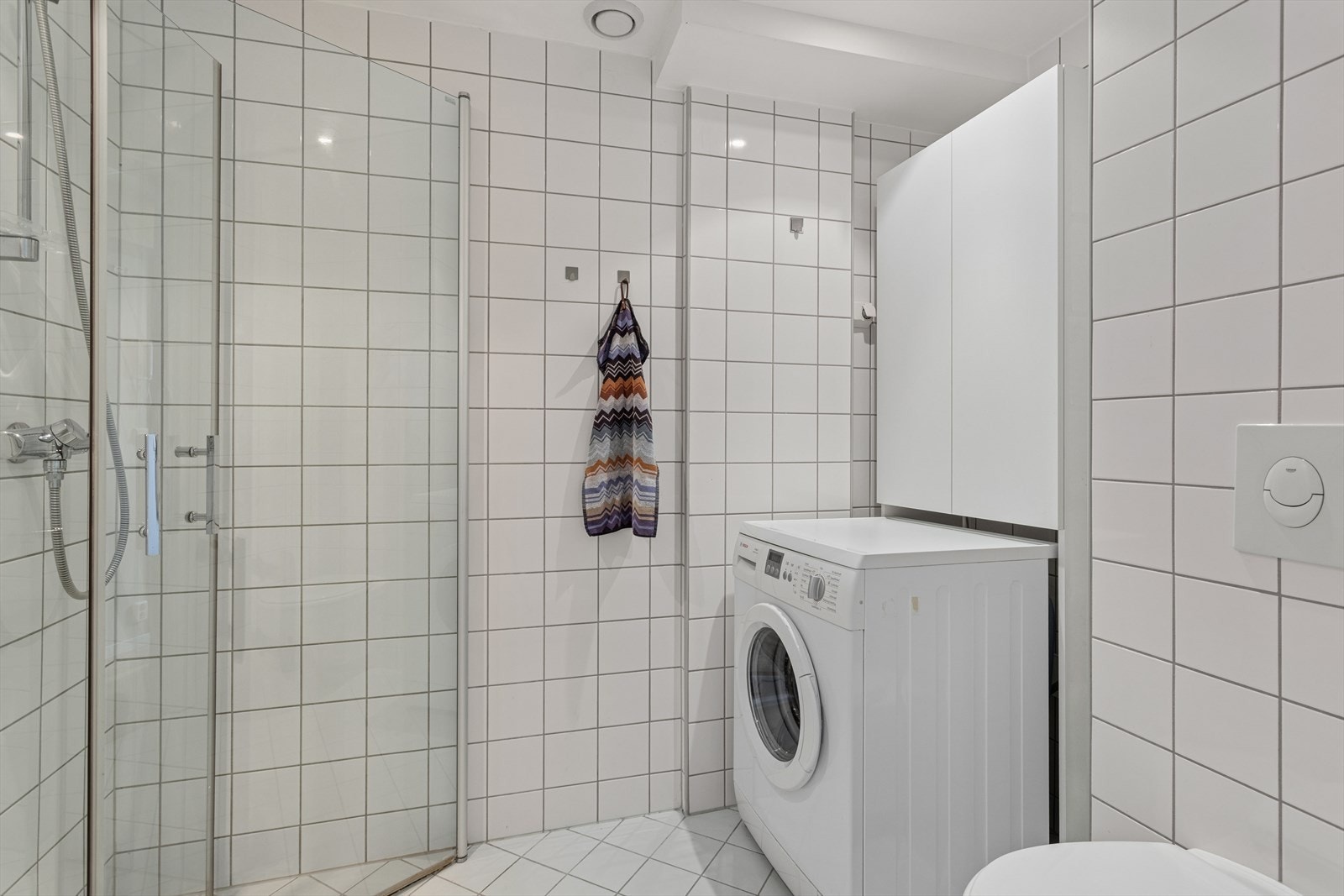 Flislagt bad med varmekabler i gulvet. Her er det dusjhjørne med innfellbare dører og opplegg for vaskemaskin. Galleribilde