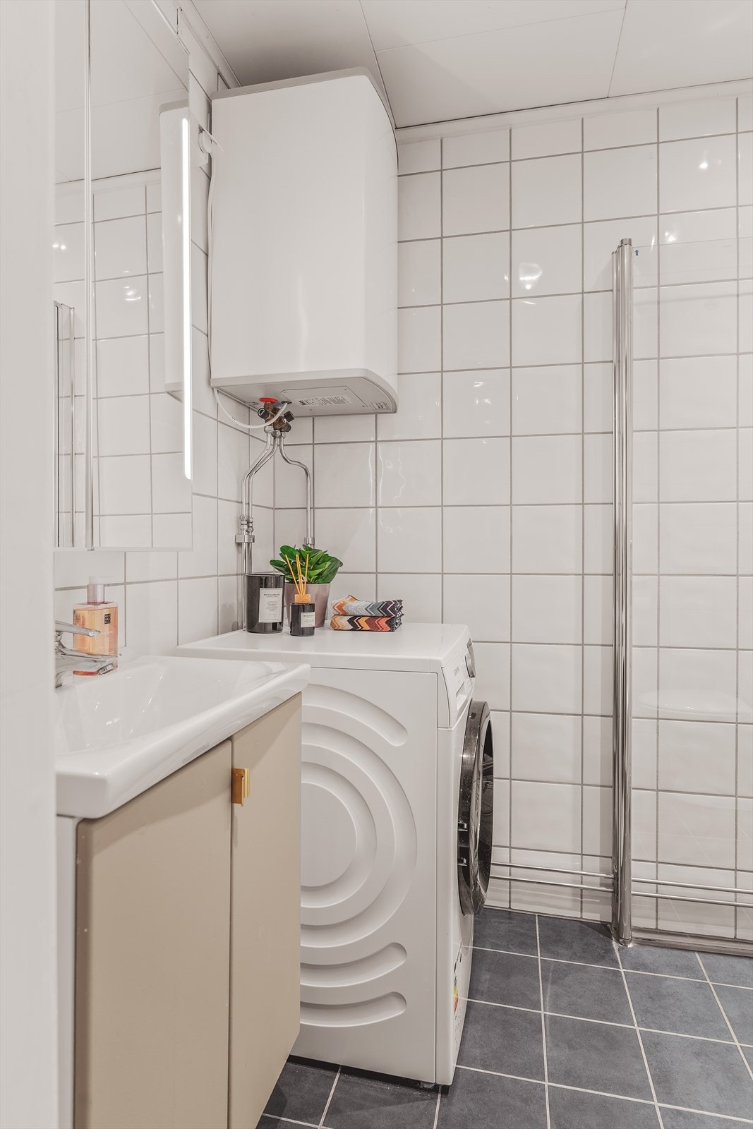 Badet er innredet med vegghengt servantskap og ovenpåliggende servant, gulvstående toalett, speilskap med belysning, og dusjsone med innfellbare glassdører. Det er opplegg for vaskemaskin. Galleribilde