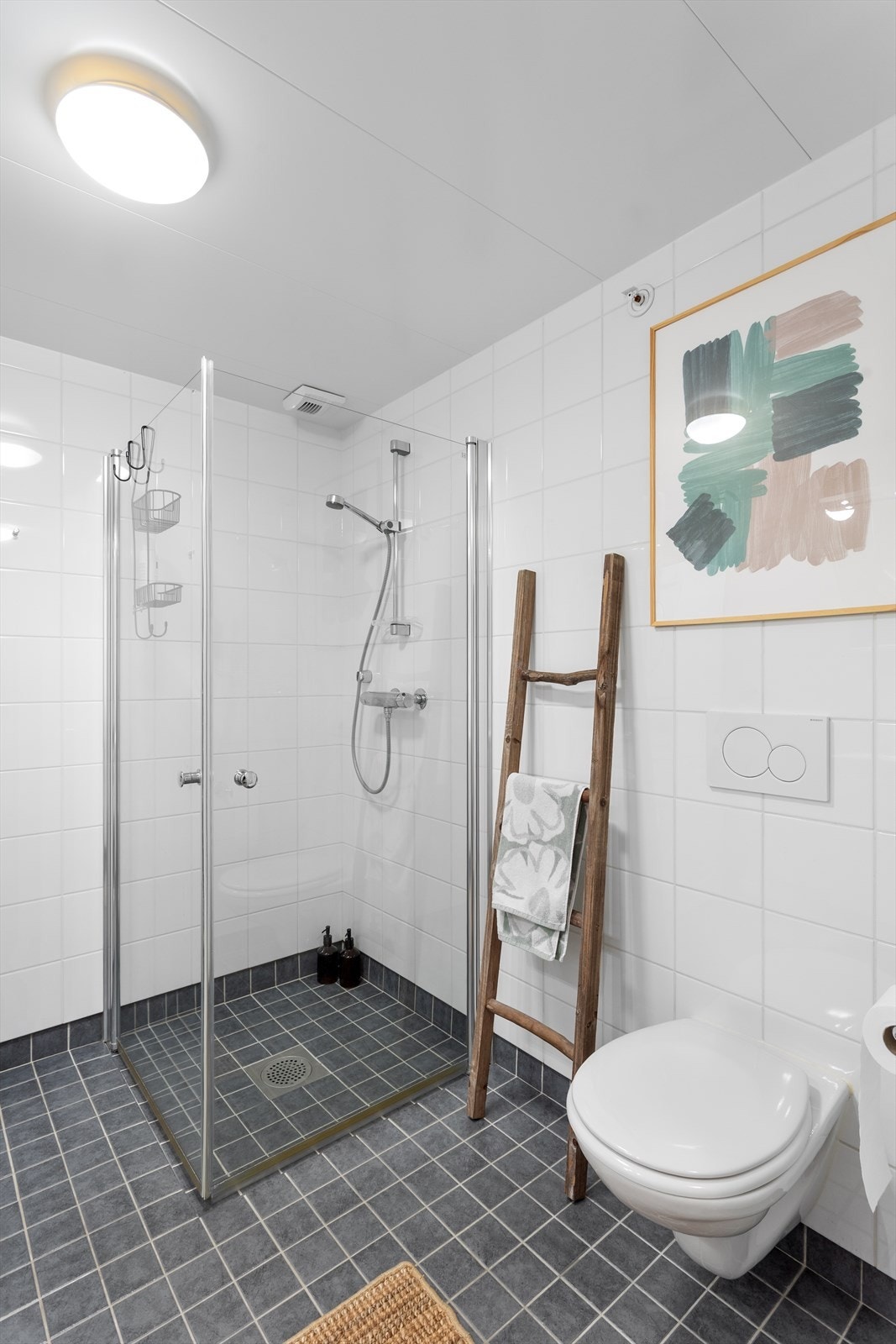 Videre er badet utstyrt med vegghengt toalett og dusjhjørne med innfellbare glassdører. Galleribilde