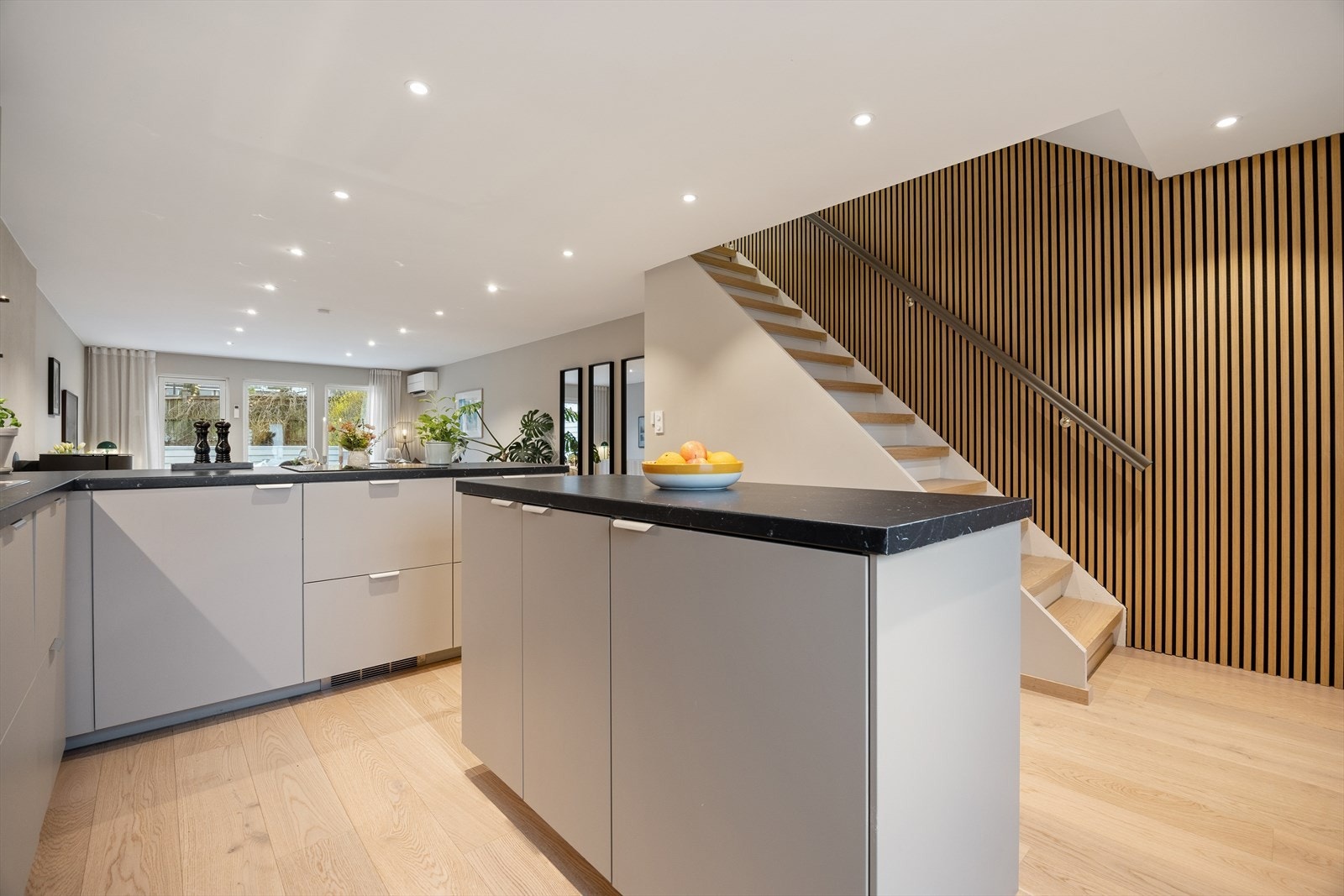 Det stilrene kjøkkenet er en integrert del av den åpne hovedetasjen. Spileveggen i eik skaper en varm og moderne overgang mot trappen. Galleribilde
