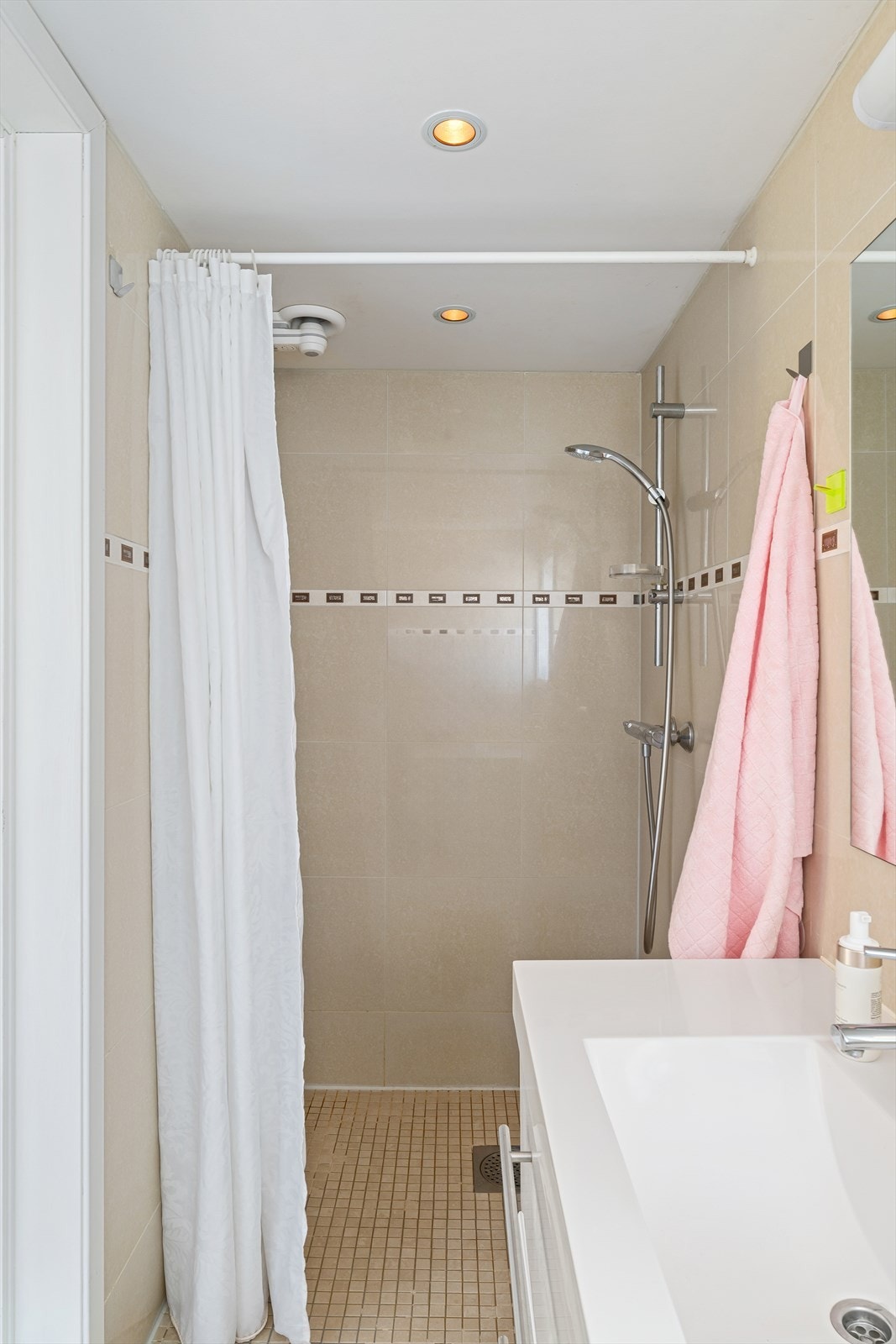 Badet er utstyrt med vegghengt toalett, baderomsmøbel med nedfelt vask og dusjhjørne med forheng. Galleribilde