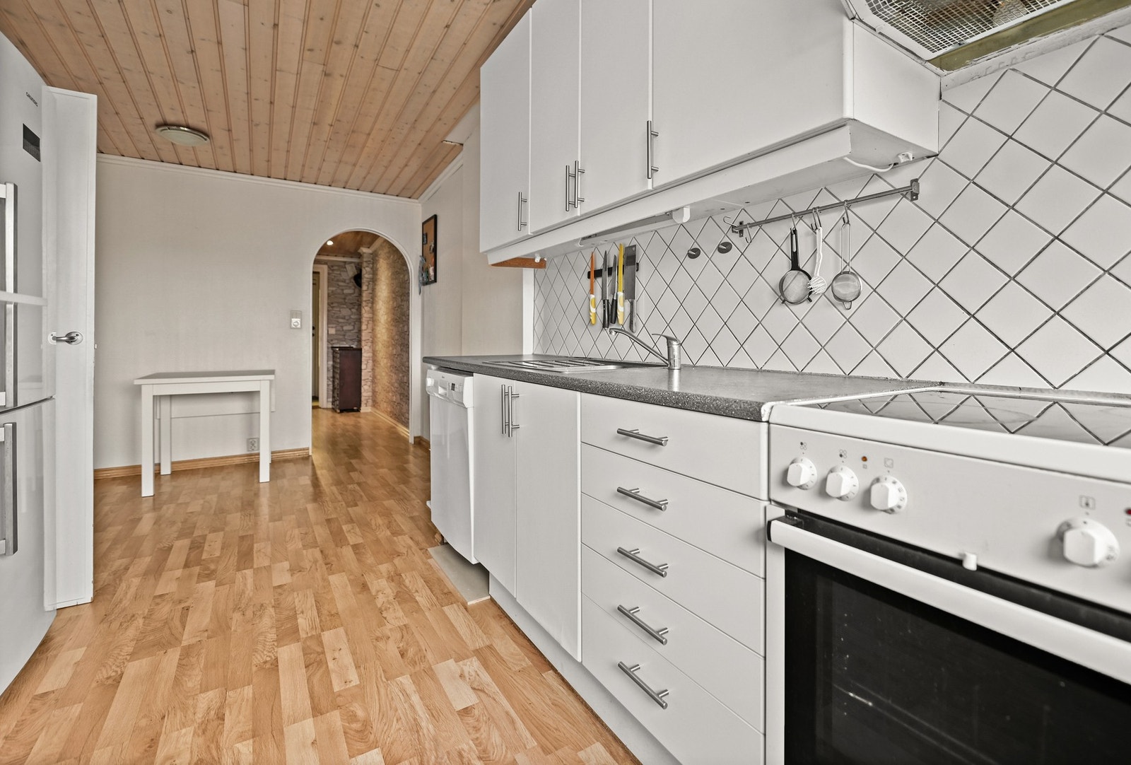 Innredningen har slette fronter, laminat benkeplate med nedfelt vaskekum og fliser mellom benkeplate og overskap. Galleribilde