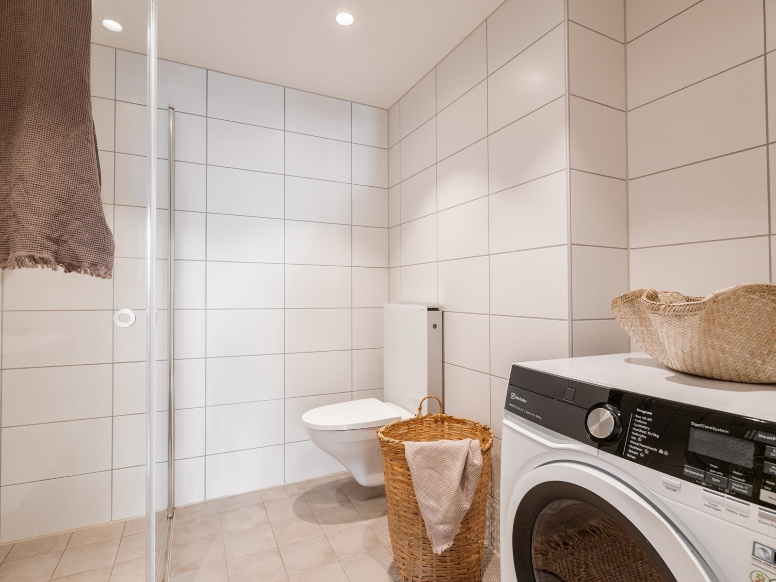 Videre er badet utstyrt med vegghengt toalett og dusjsone med innfelte dusjdører i herdet glass. Galleribilde