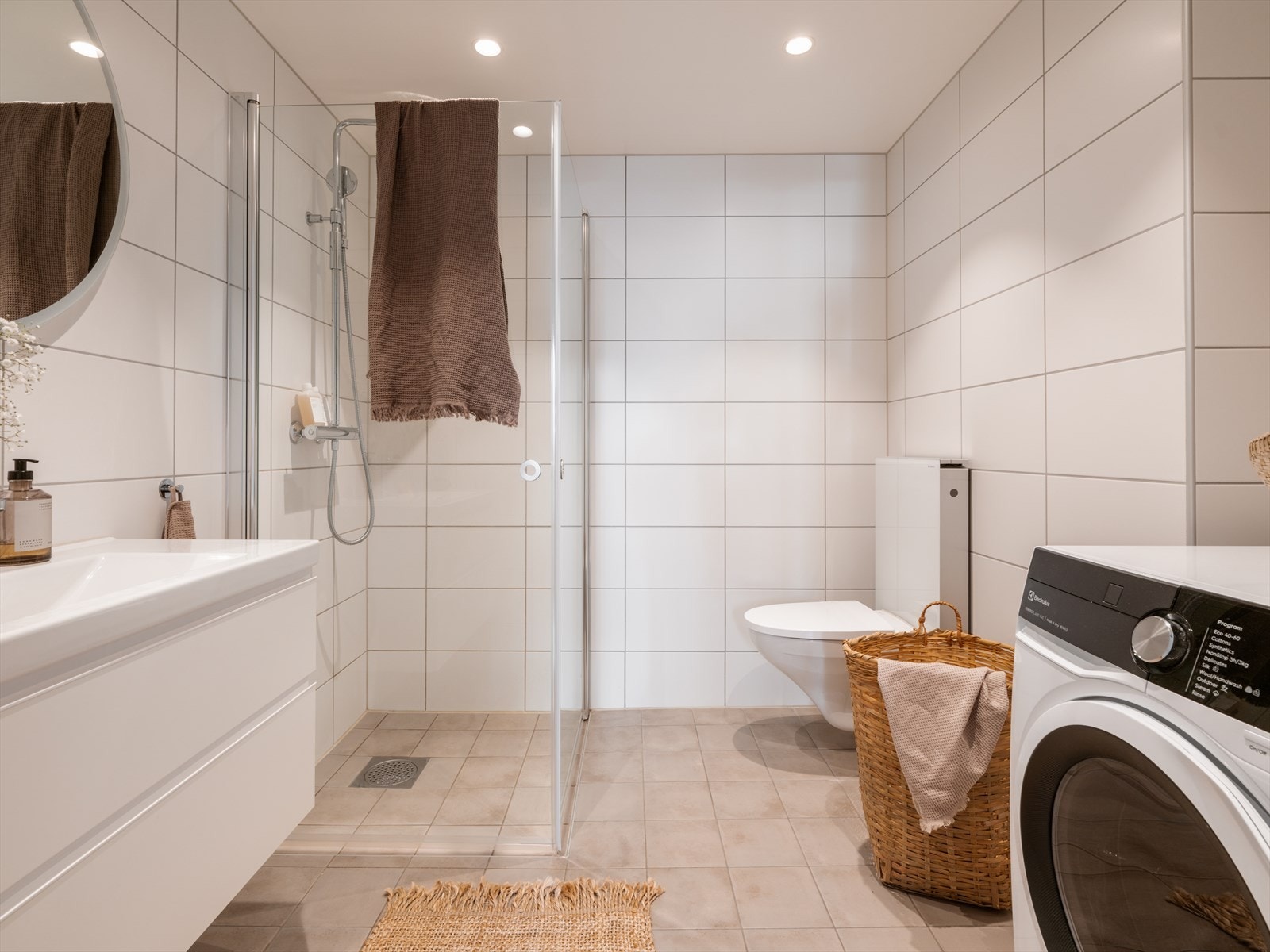 Badet er romslig og helfliset med fliser på både gulv og vegger, noe som gir et tidløst uttrykk. Det er opplegg for vaskemaskin. Gulvet er utstyrt med varmekabler, og himlingen er nedsenket med innfelte downlights som gir jevn og behagelig belysning. Galleribilde