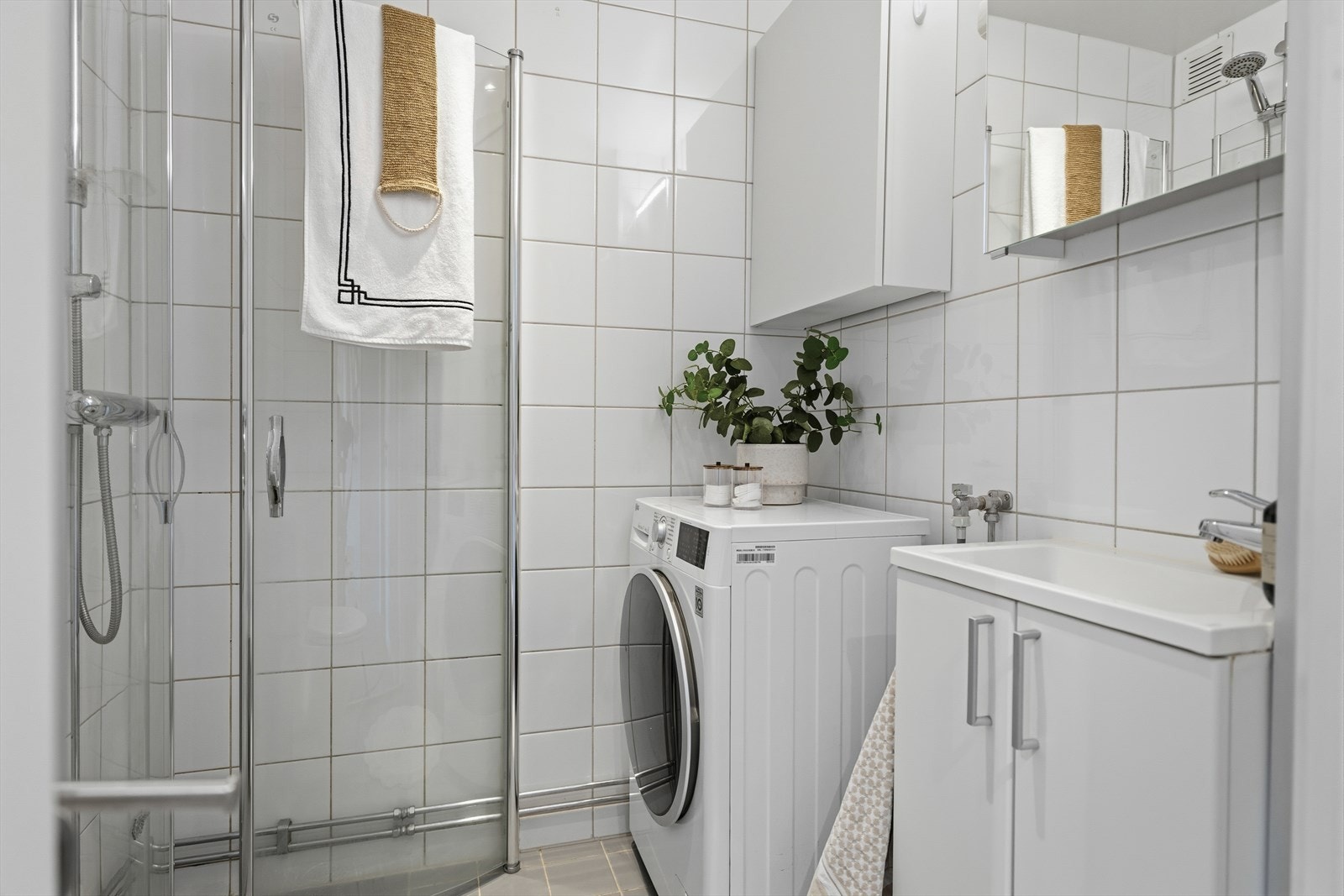 Flislagt bad med varmekabler i gulv og senket, malt platehimling med downlights. Badet er utstyrt med et gulvmontert toalett, servant med underskap, speilskap over servant og et veggskap. Galleribilde